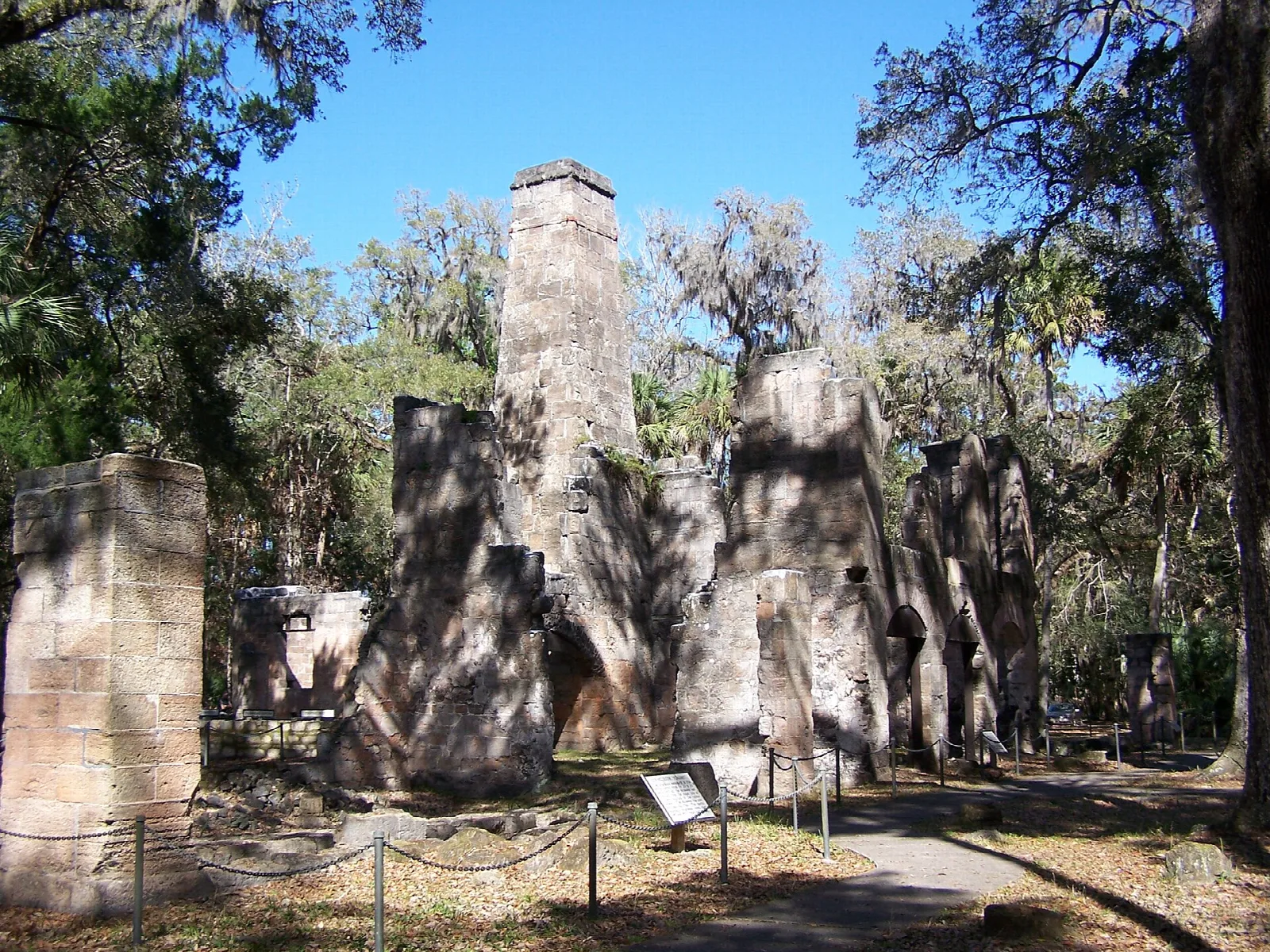 Tall stone ruins of a sugar mill among oaks and palms