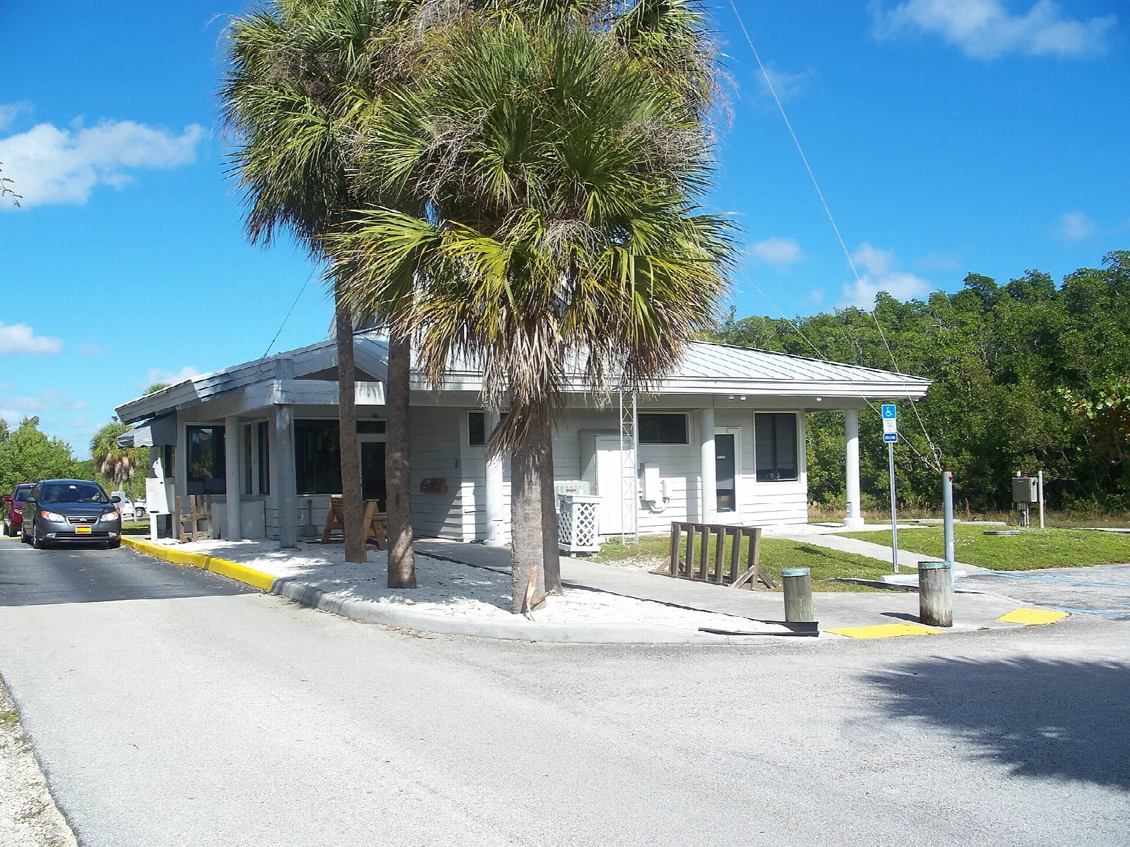 Small white building with a porch beside a road and palms