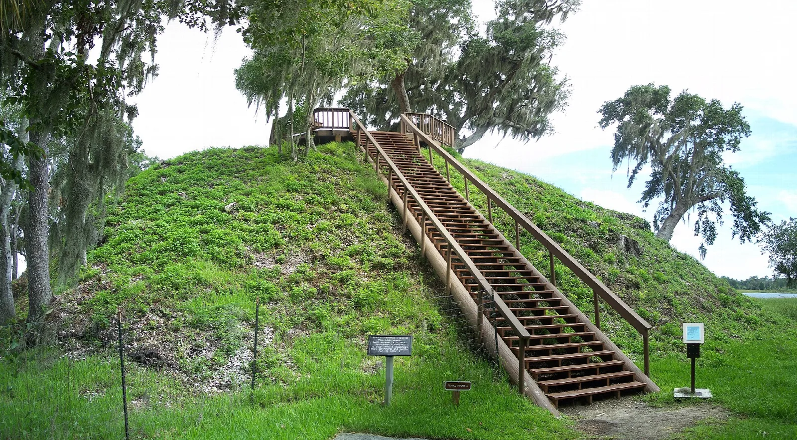Steep grassy mound with a wooden stairway and railing