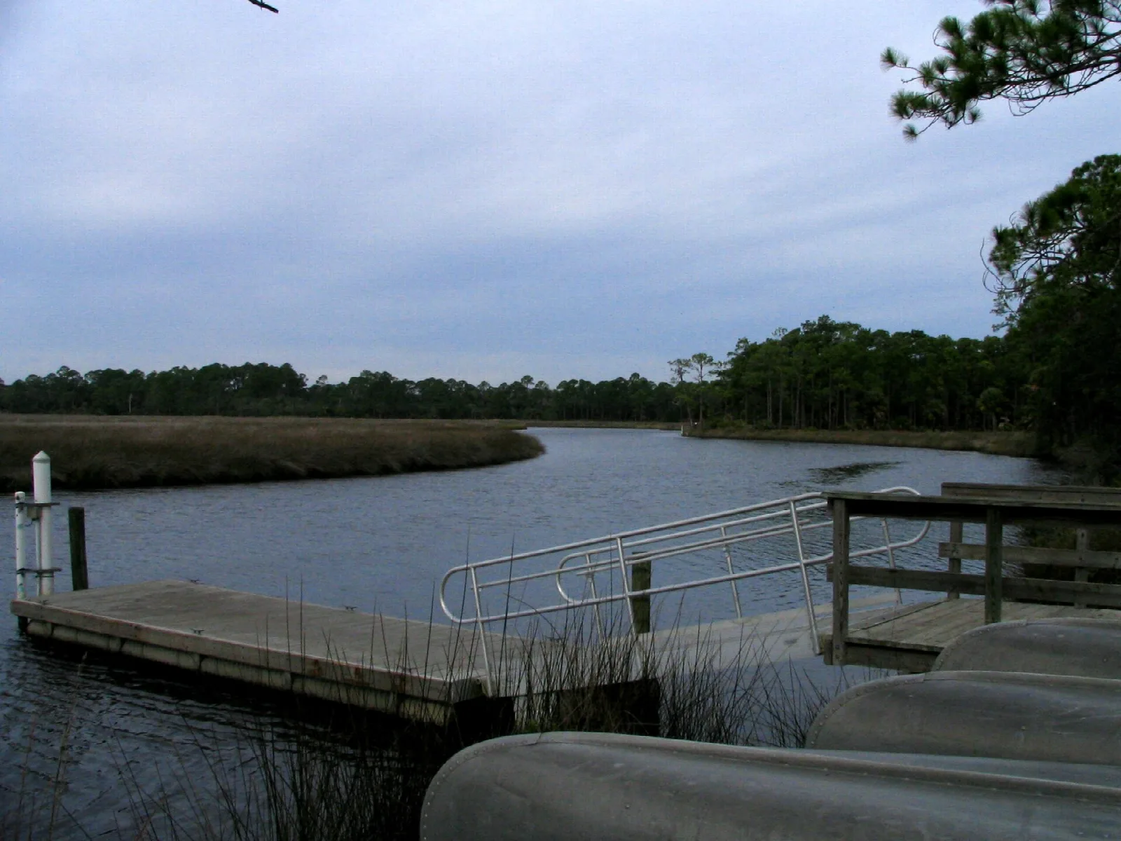 Wooden dock with a rail and boats beside a creek