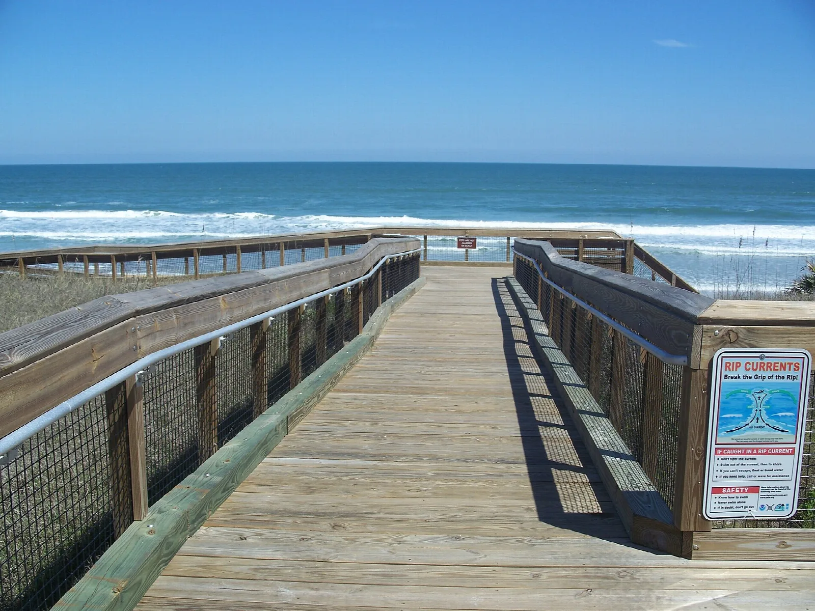 Wooden boardwalk with rails and a safety sign above the surf