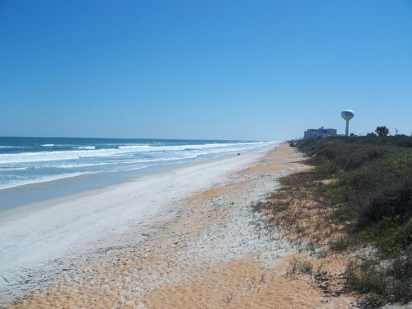 Long sandy beach with surf and dunes under a blue sky