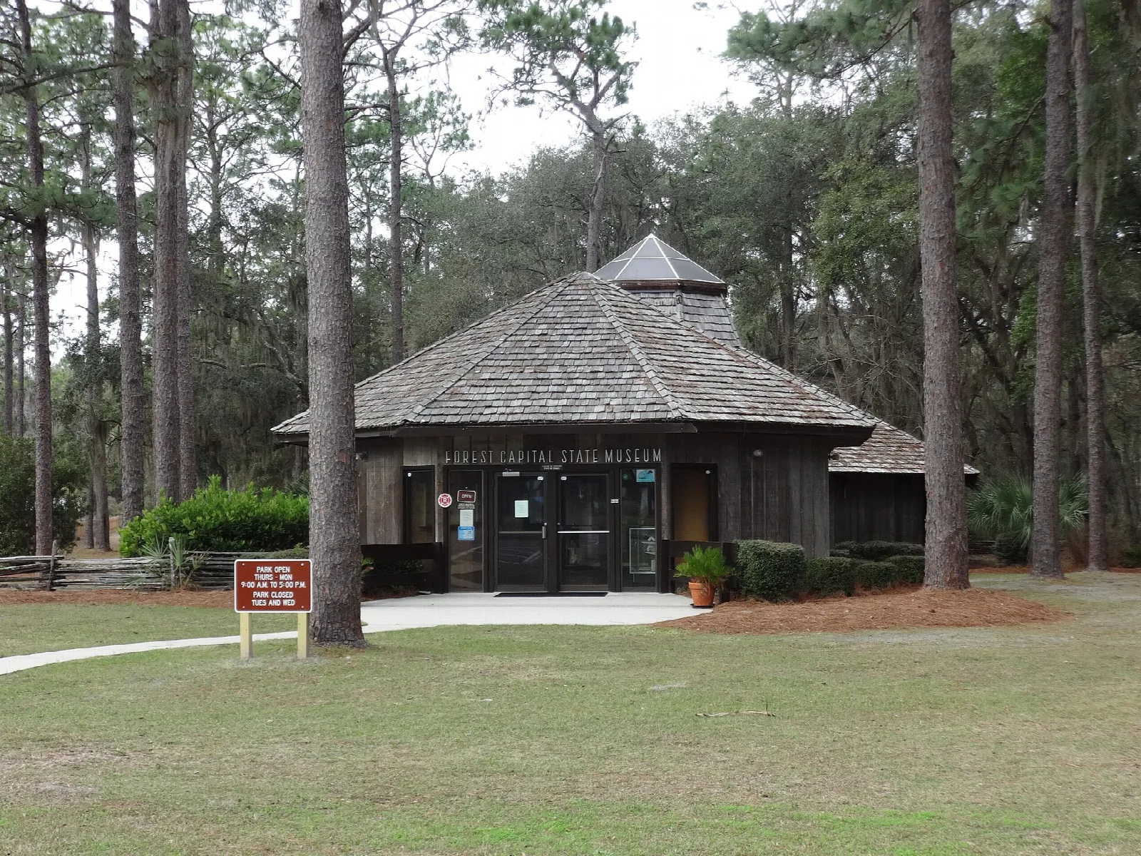 Small wood-shingle museum building under tall pines