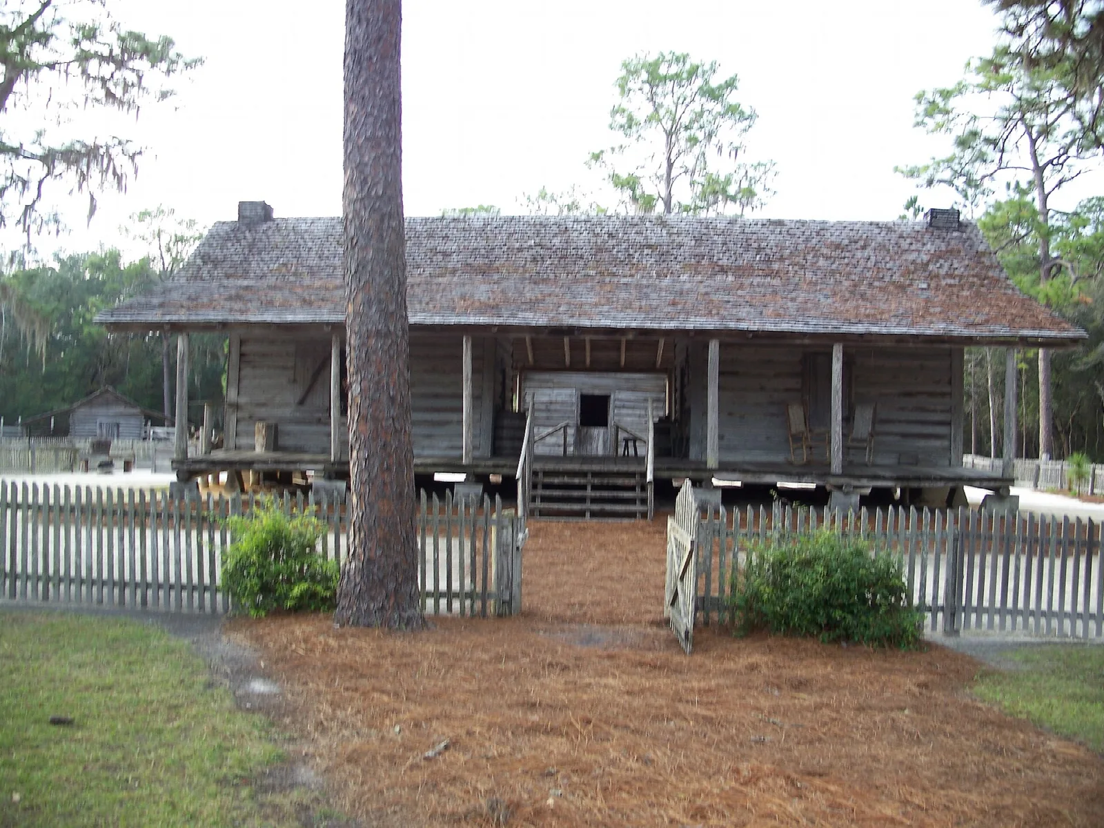 Raised wooden farmhouse with a porch and picket fence among pines