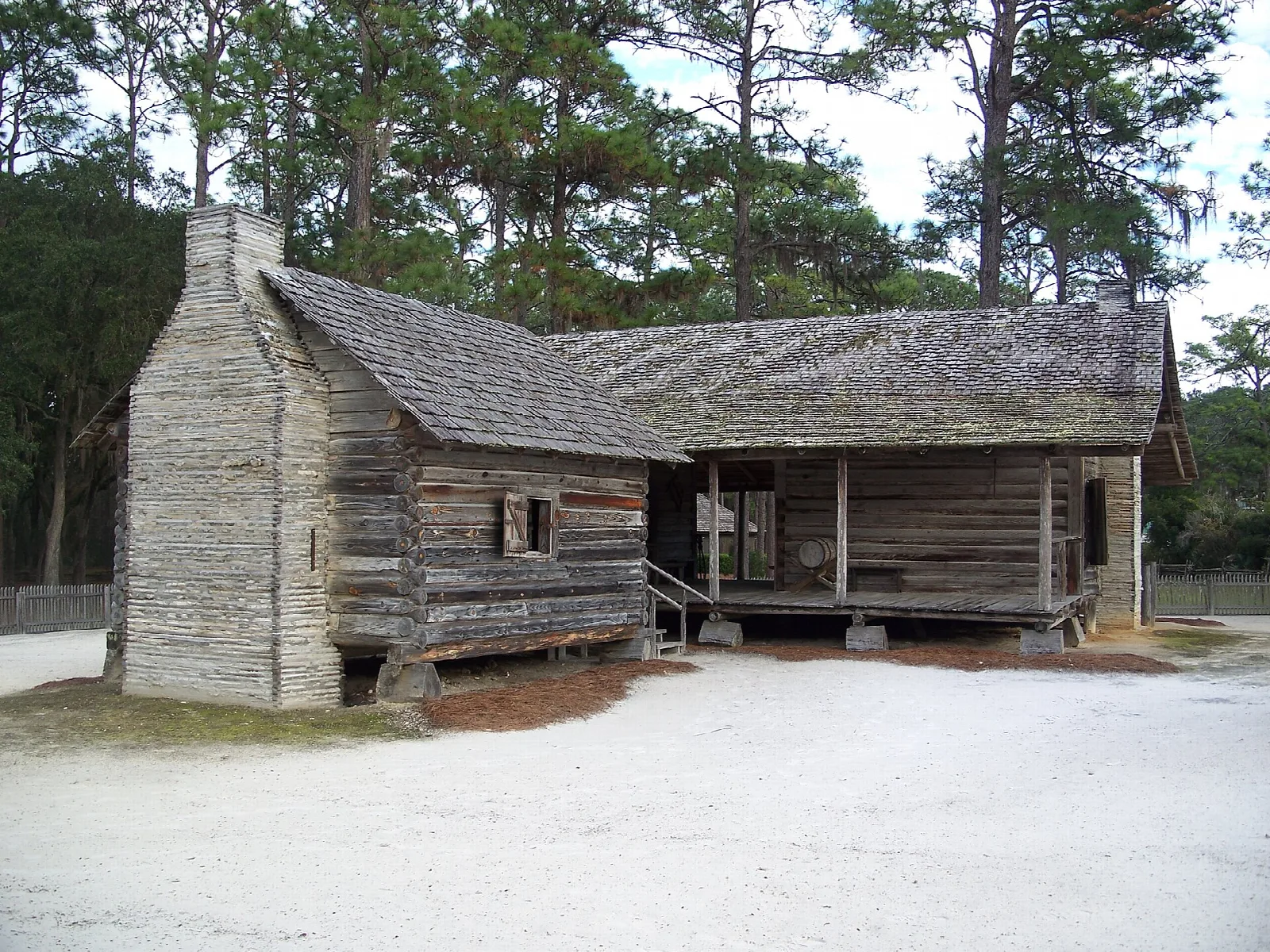 Weathered log cabin with a stone chimney and porch, part of the Cracker homestead
