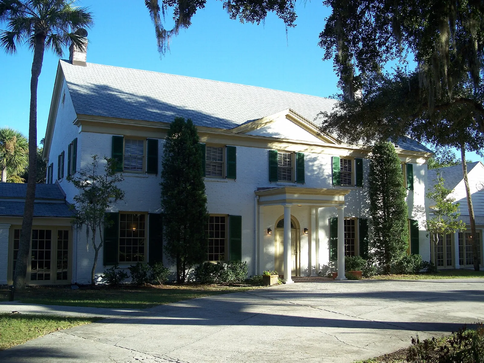 Large white colonial-style clubhouse with green shutters and palms
