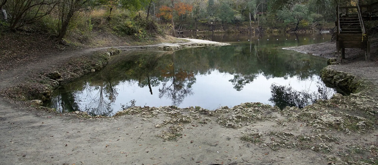 Round spring pool in a sandy bowl with a wooden stair at the edge