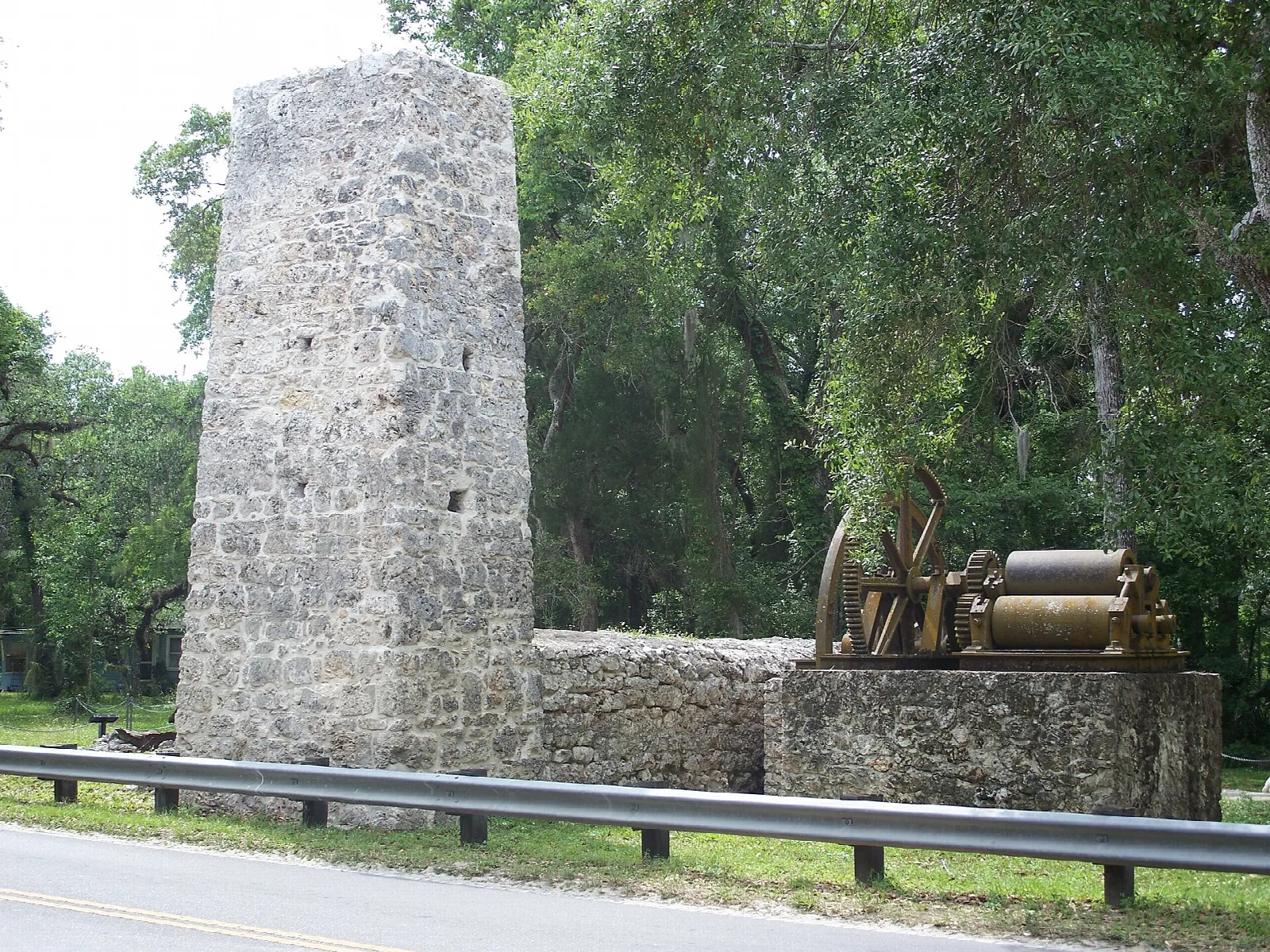 Tall stone chimney beside a road under oak trees