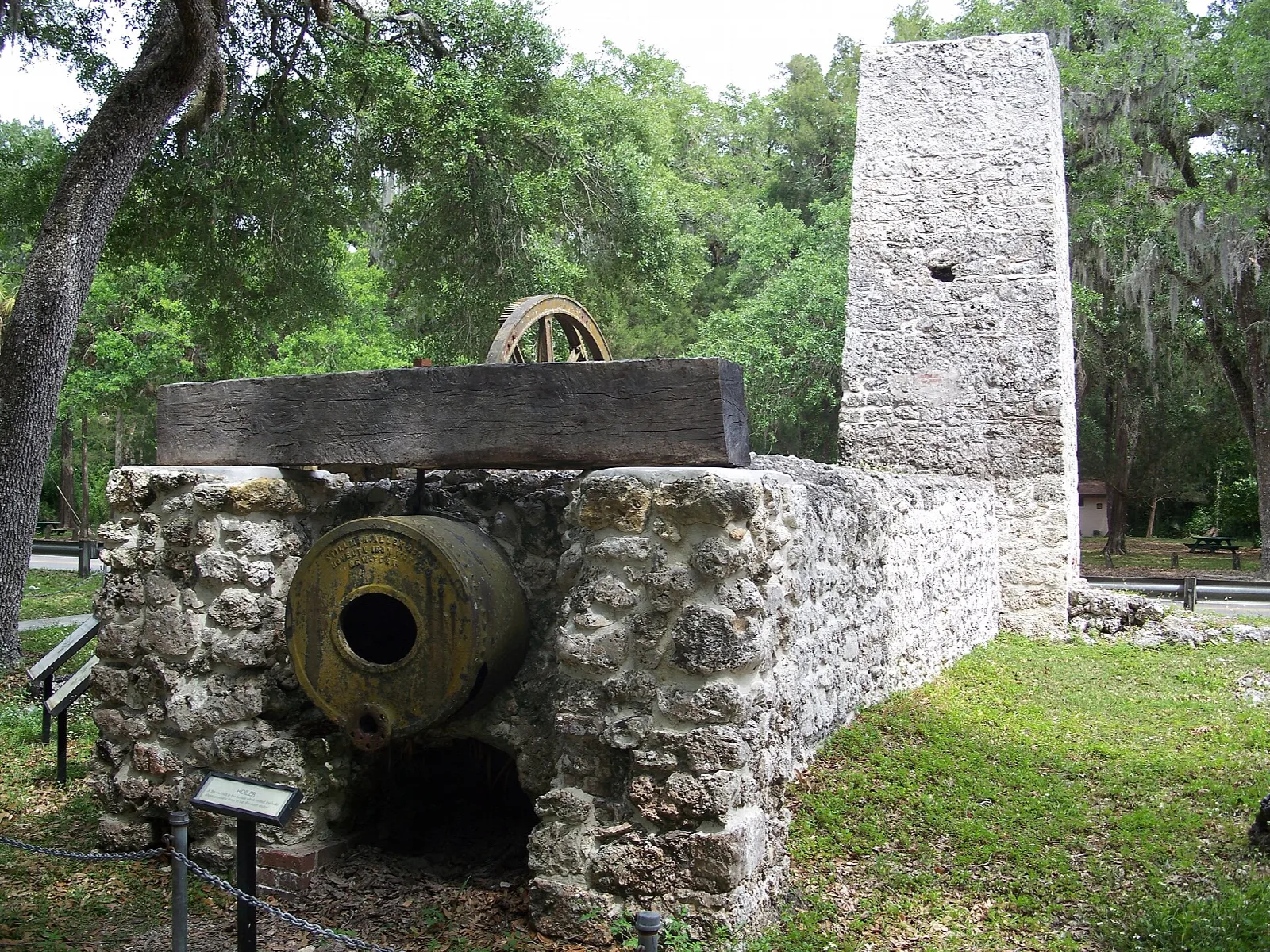 Stone sugar mill chimney behind an old iron boiler and low stone wall