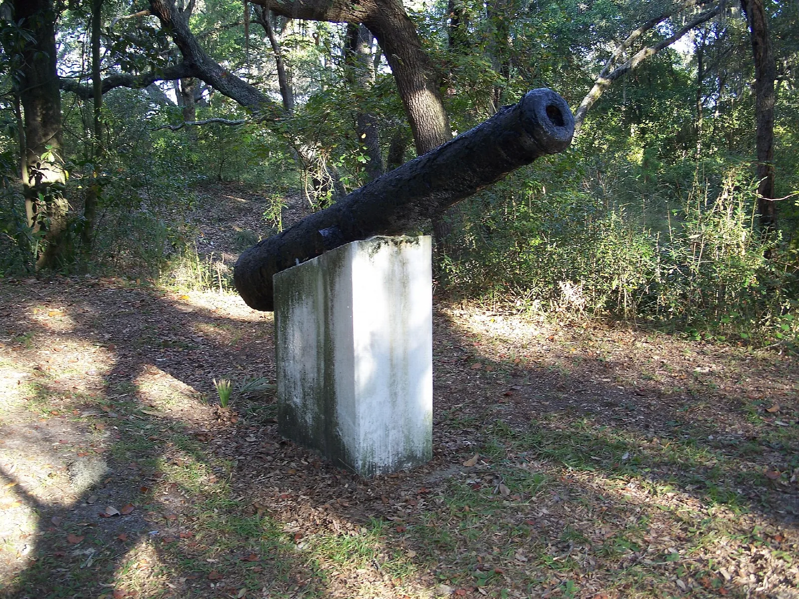 Old iron cannon on a white post among trees