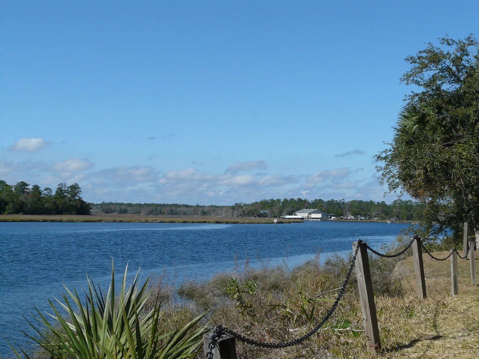 Wide river with distant shore seen past a chain fence