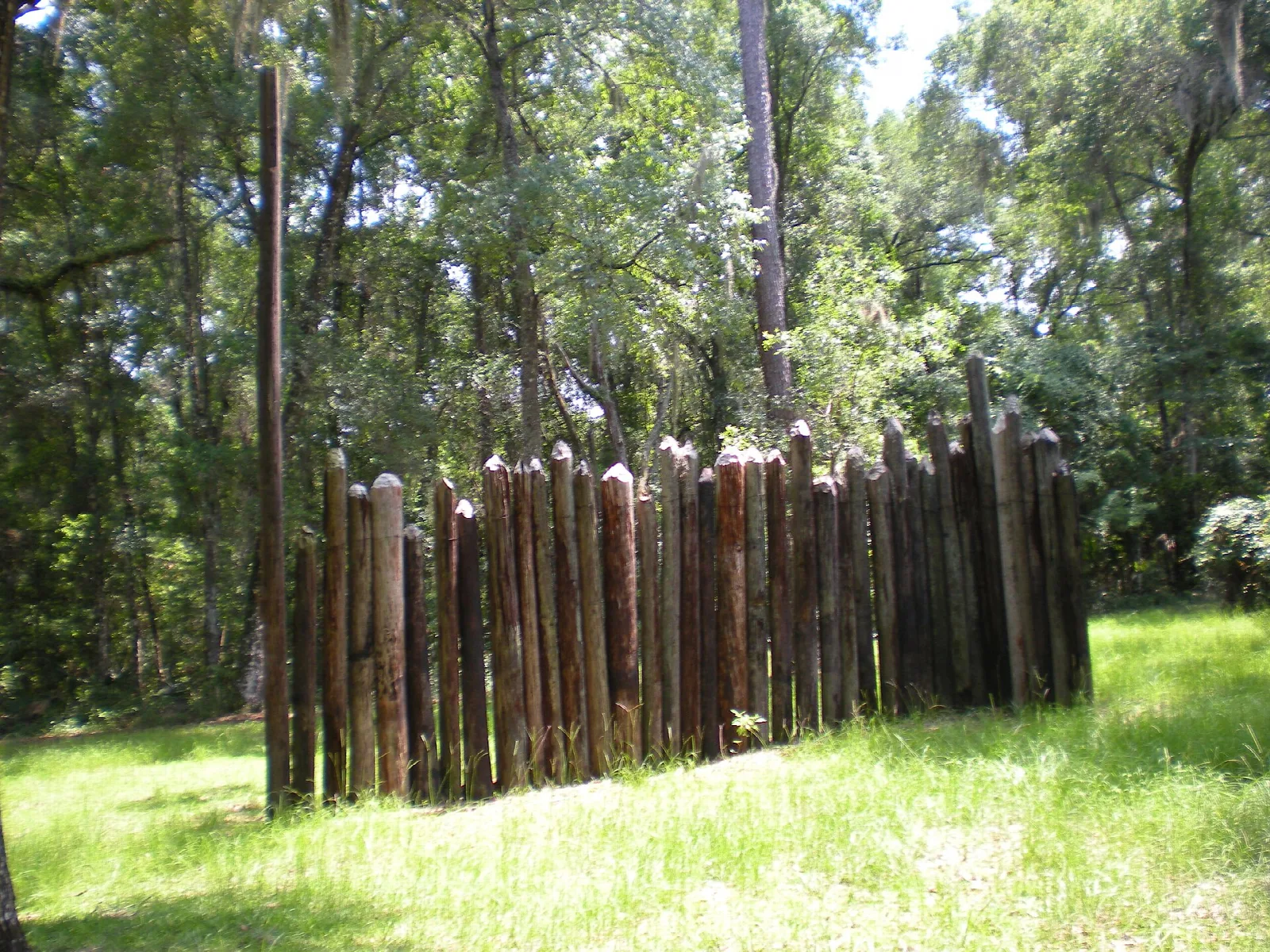 Wooden log stockade wall rising from a green lawn