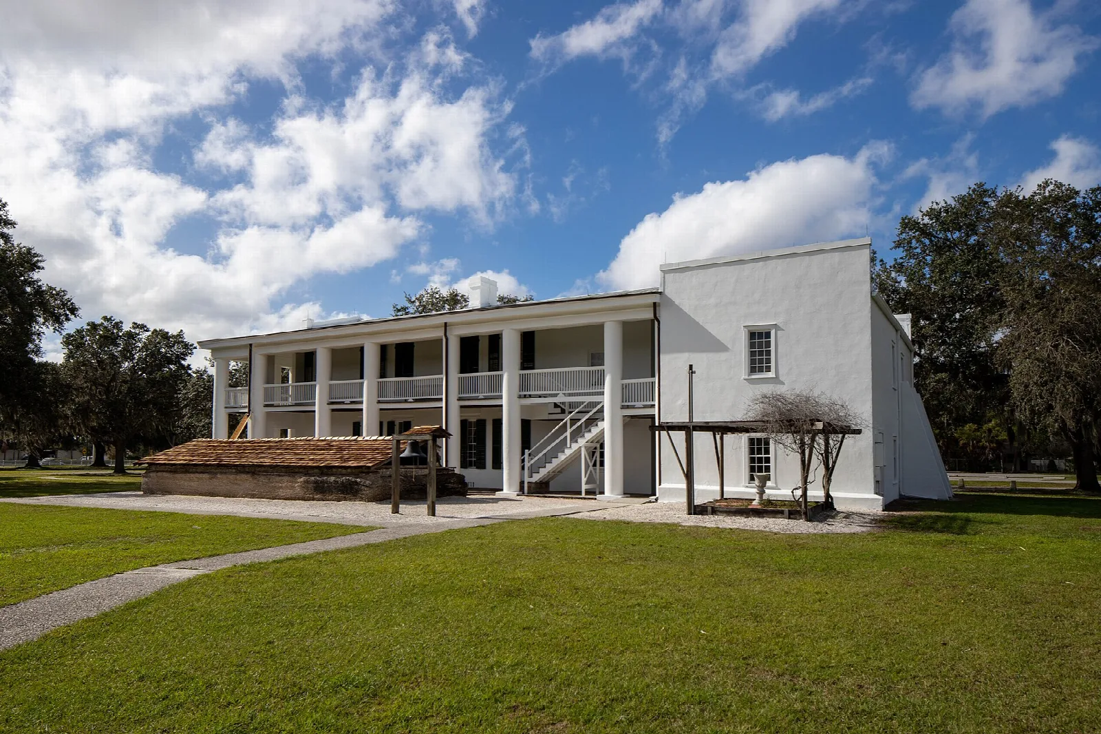 Two-story mansion with upper porch under blue sky and clouds
