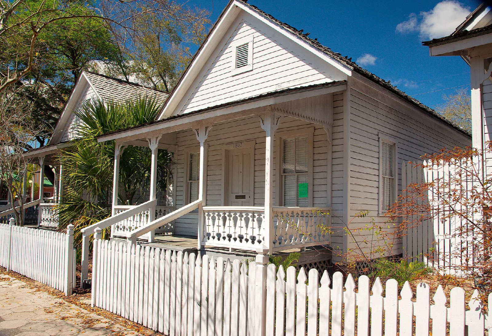 White wooden cottage with a front porch and picket fence