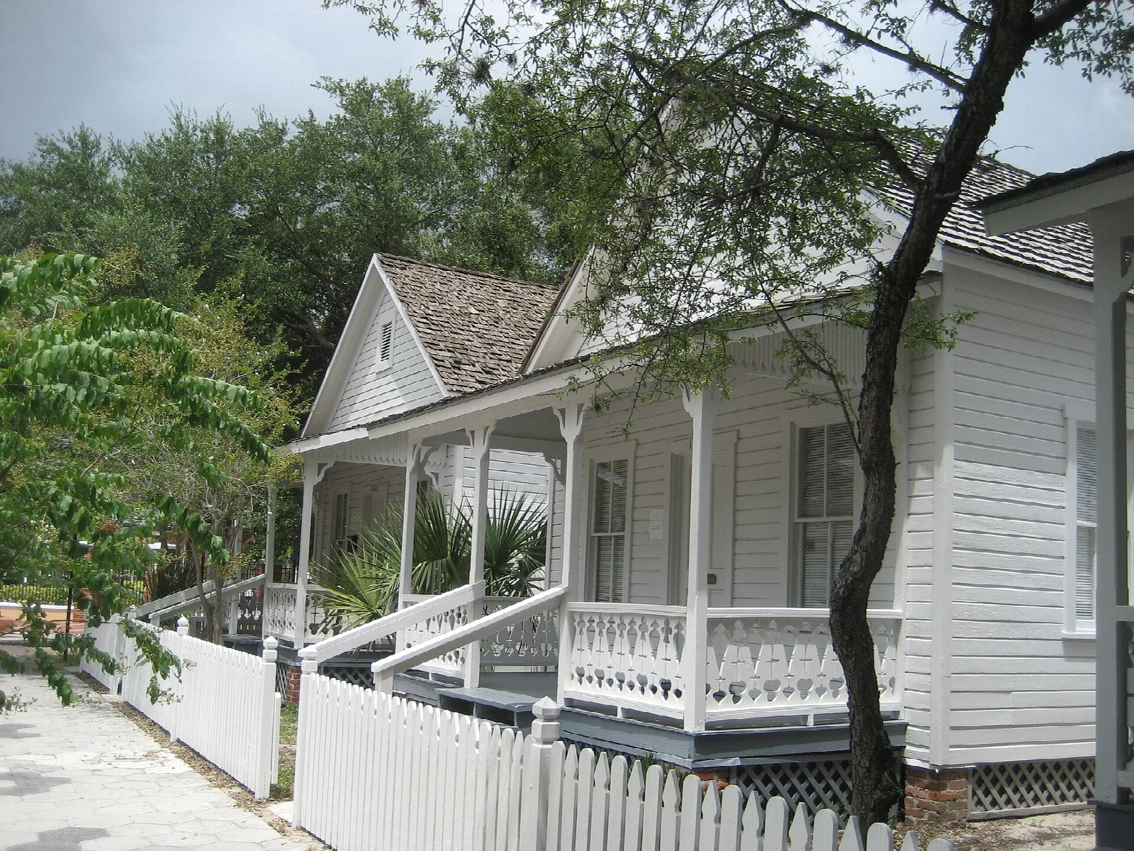 White wooden cottage with a porch behind a picket fence
