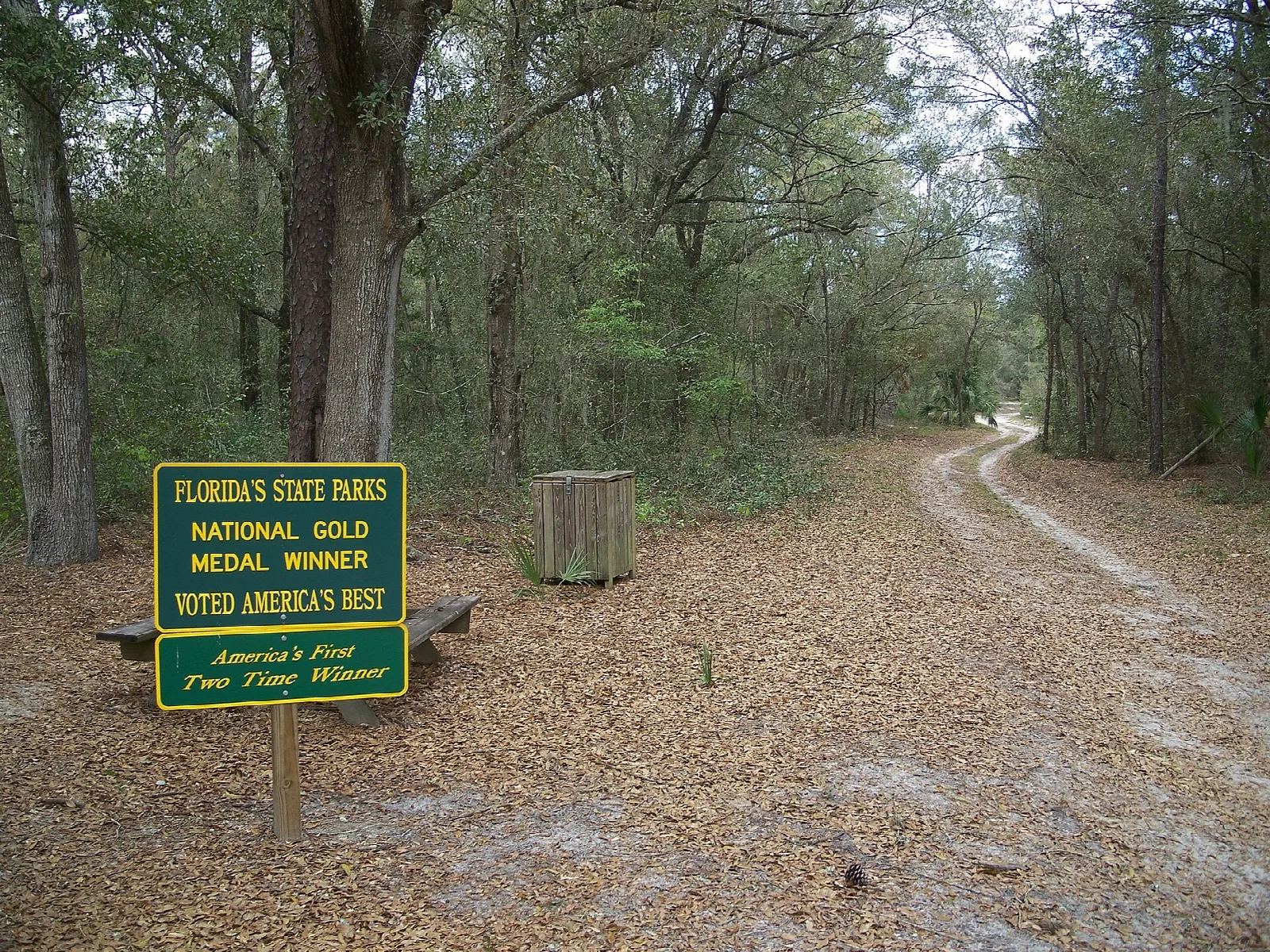Dirt road into shady woods with a small green sign at the side