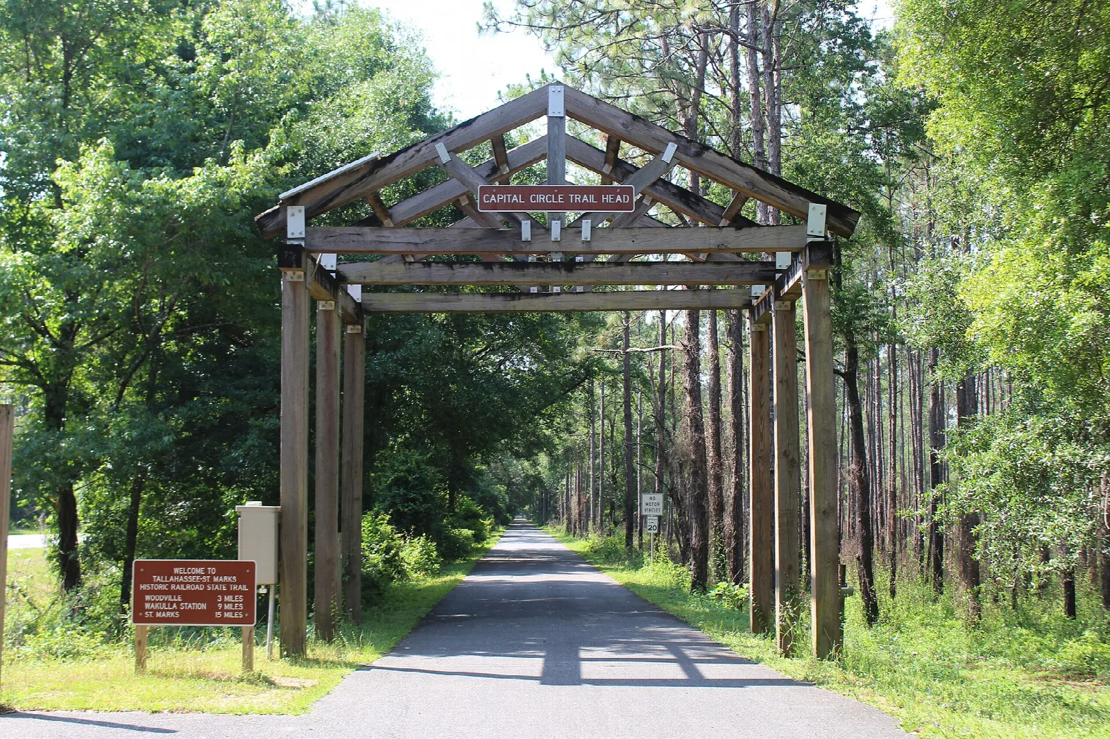 Wooden trailhead arch over a paved trail in pine woods