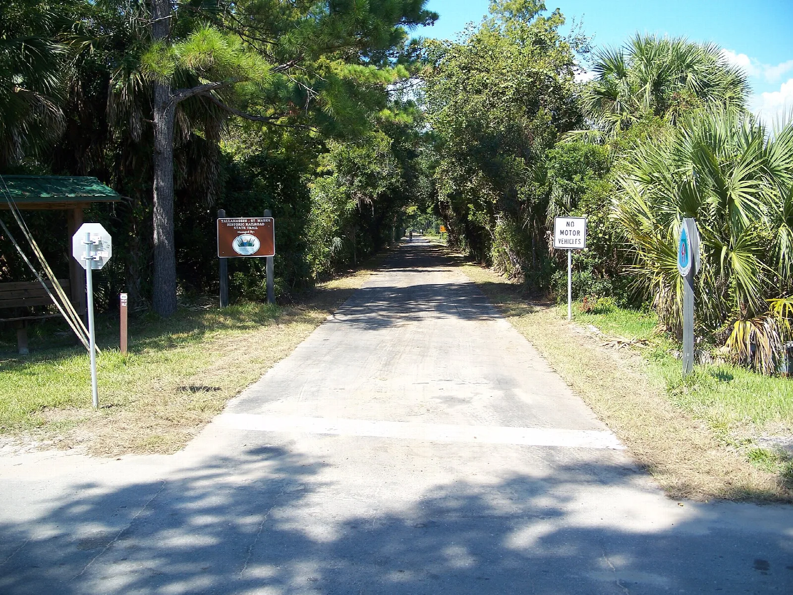 Paved trail with signs between palms