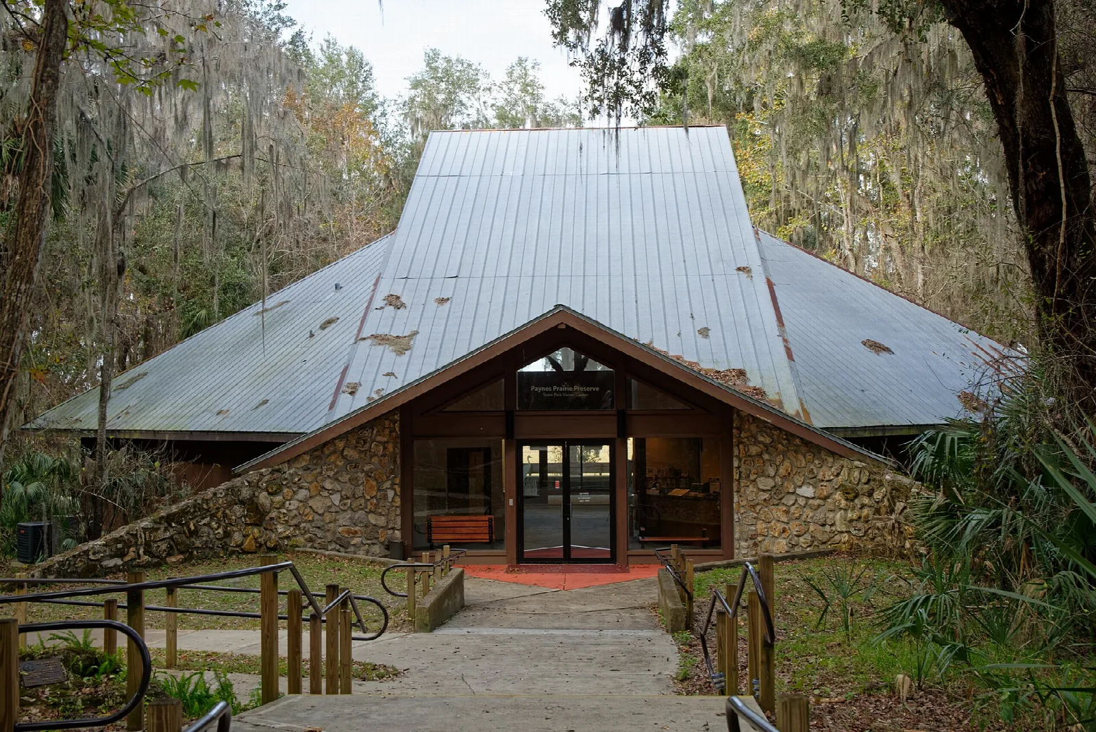 Stone-and-glass visitor center with a metal roof under moss-draped oaks