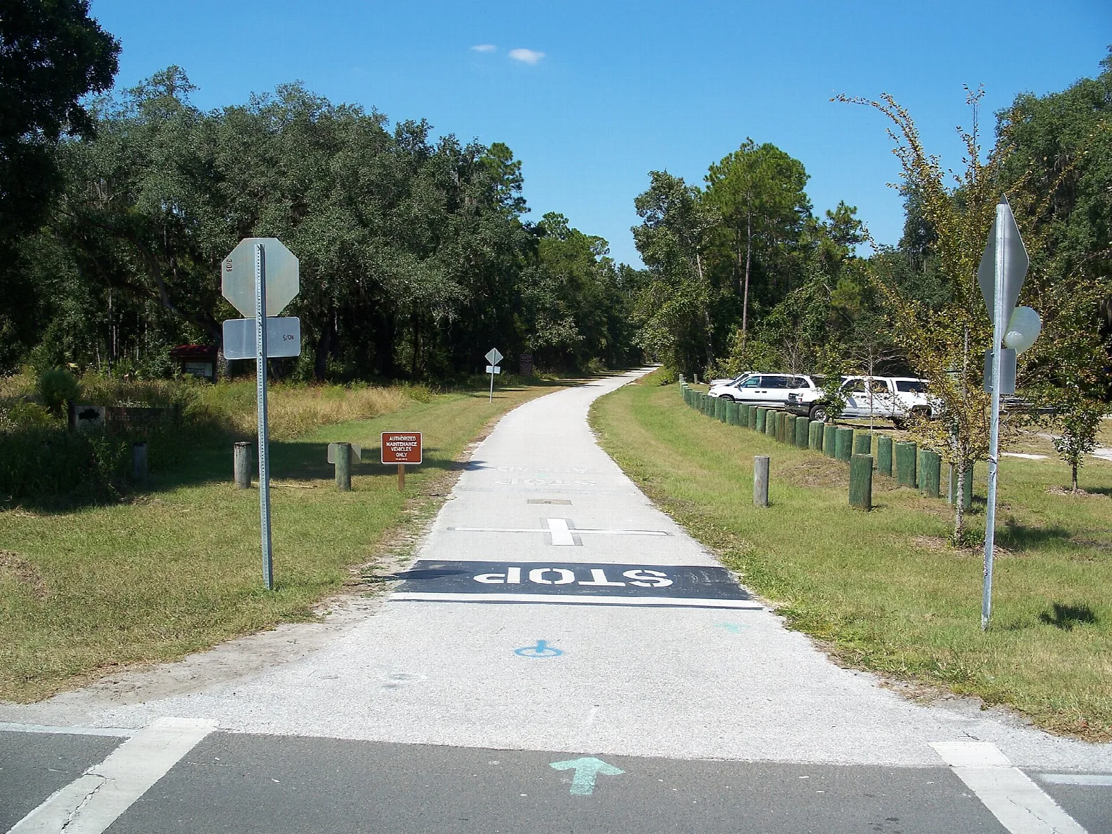 Paved trail crossing grass toward trees at a road
