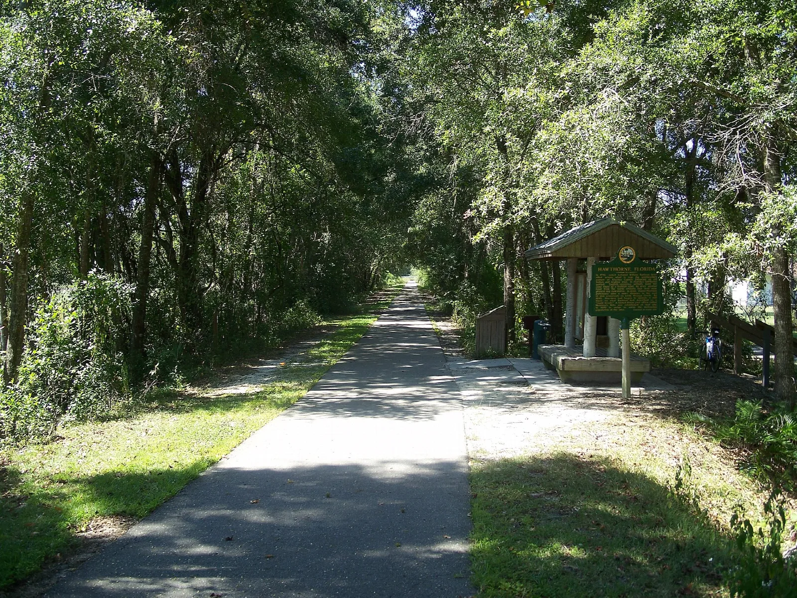Paved trail beside a small covered kiosk under trees