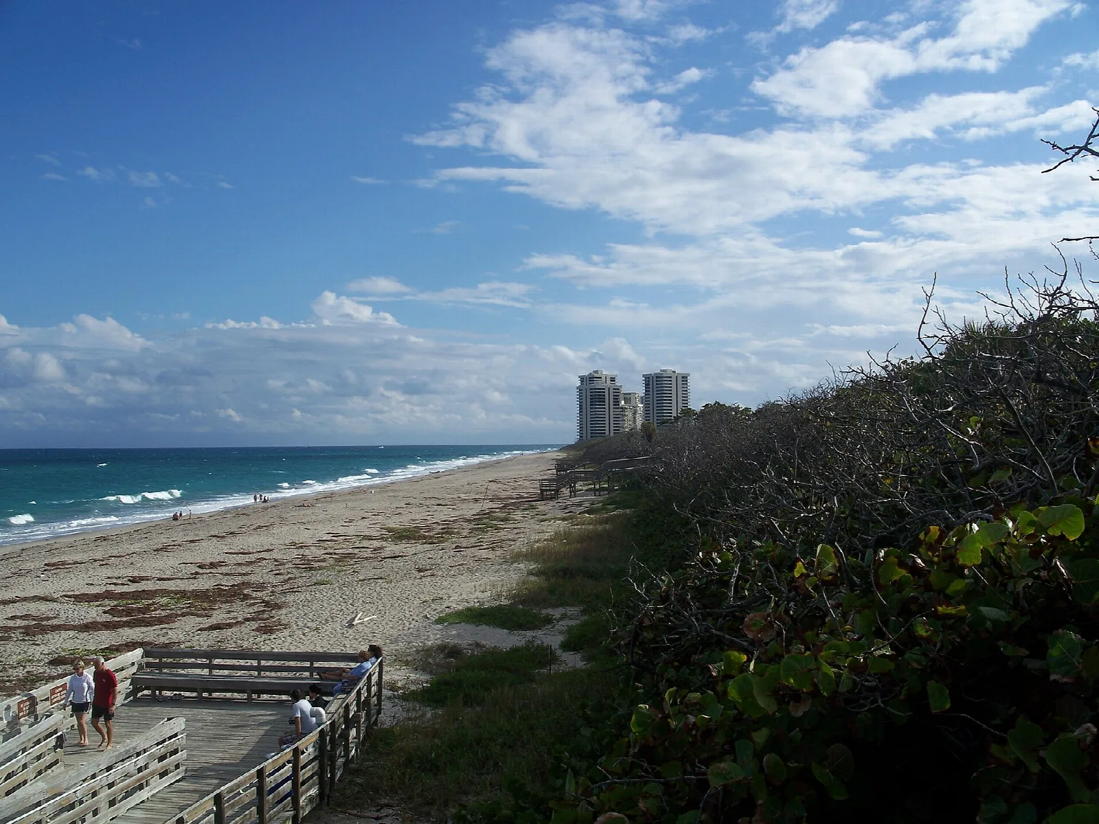 Beach below a dune with a boardwalk and distant buildings
