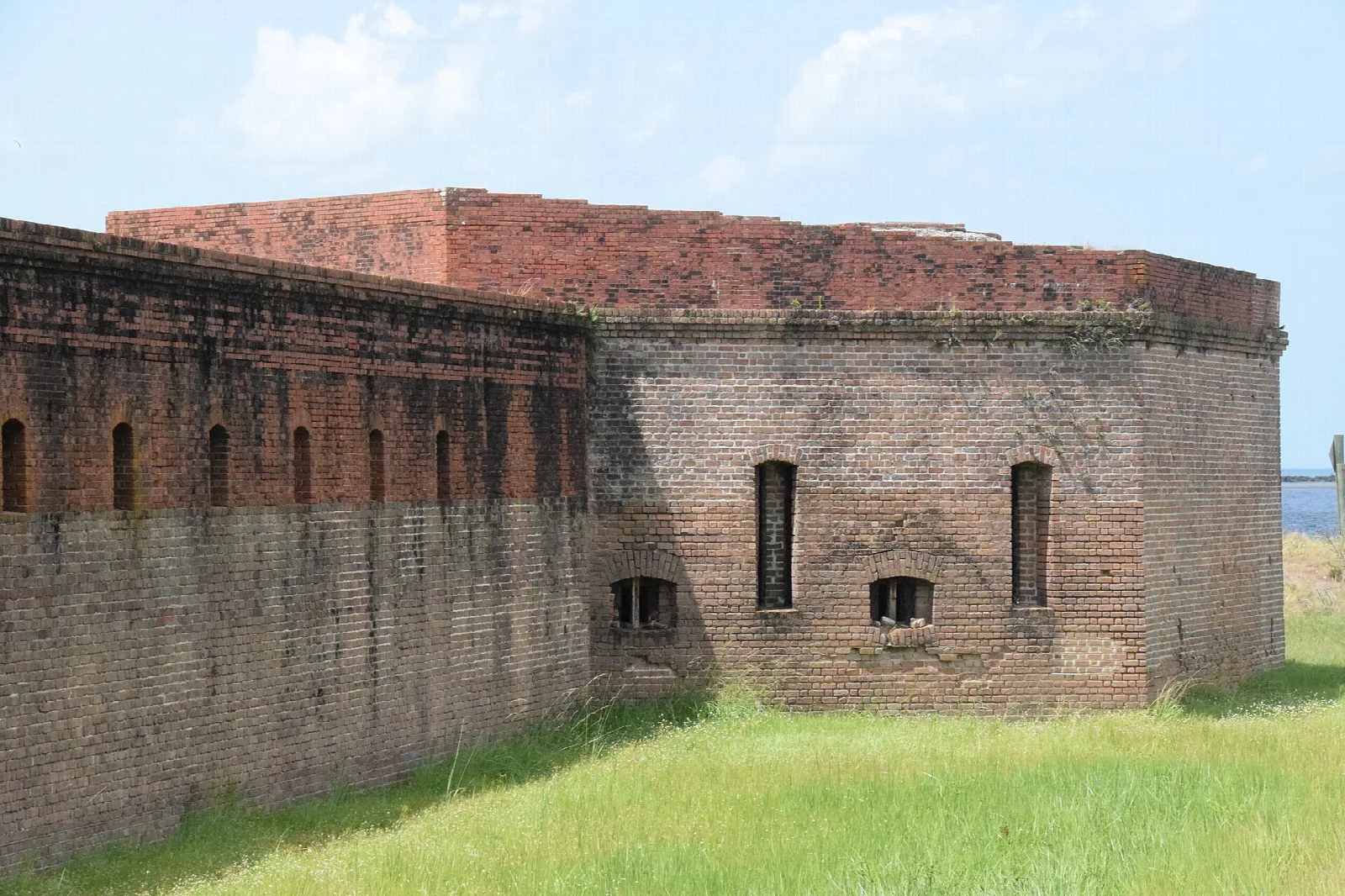 Large brick fort wall with arched openings and grass in front