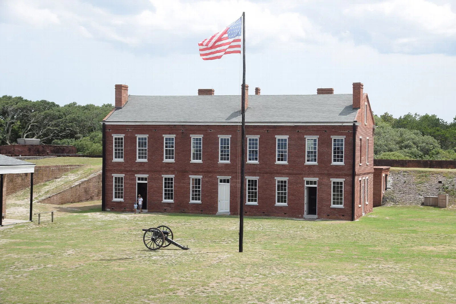 Red brick fort building with a flagpole and cannon on a lawn