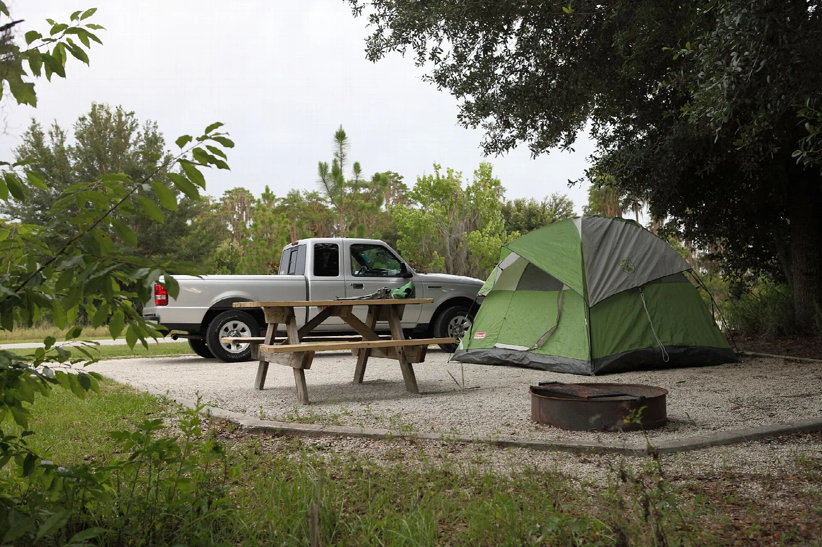 Campsite with picnic table, fire ring and a green tent under trees