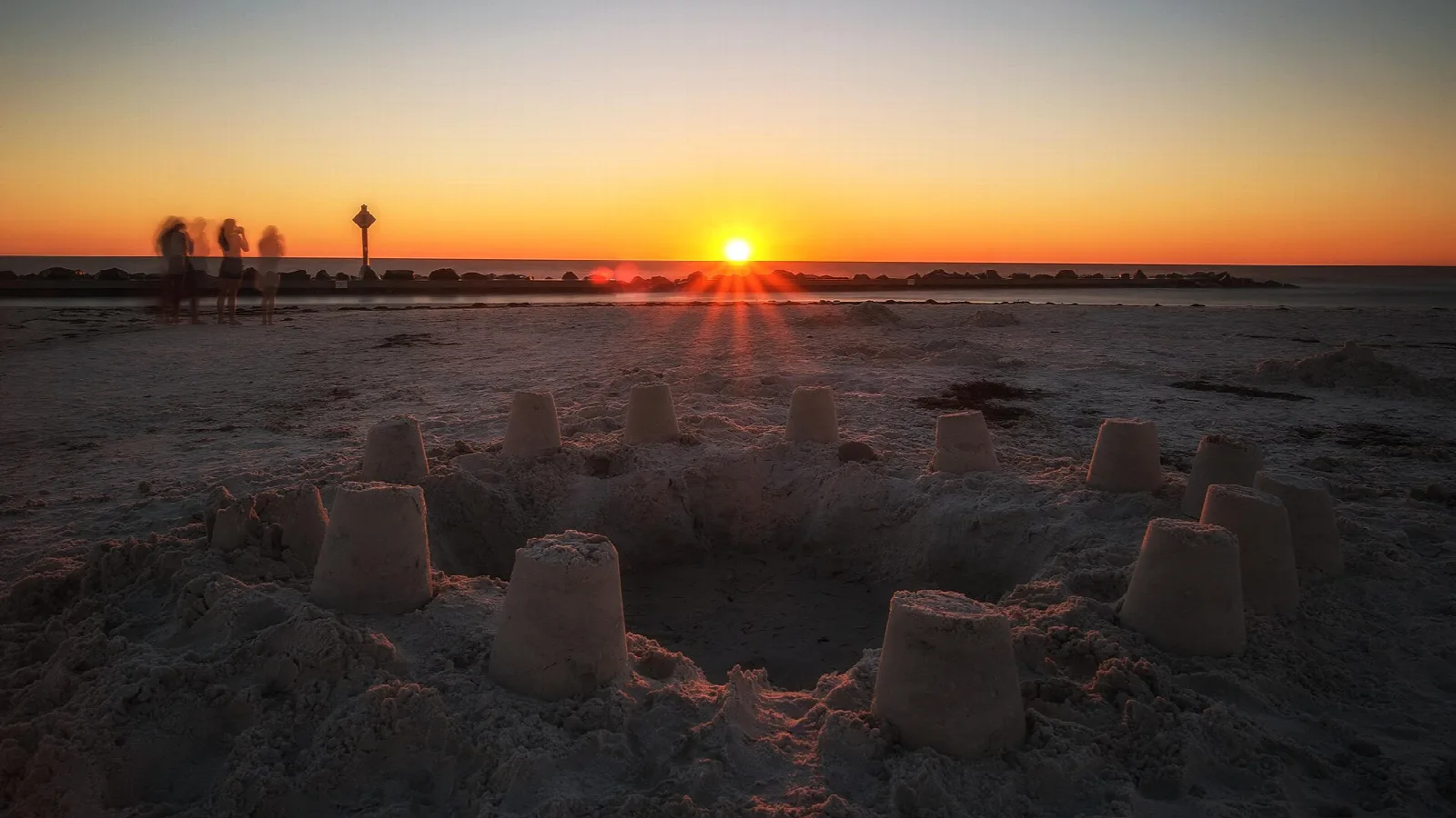 Sun setting over water behind sandcastles on a beach