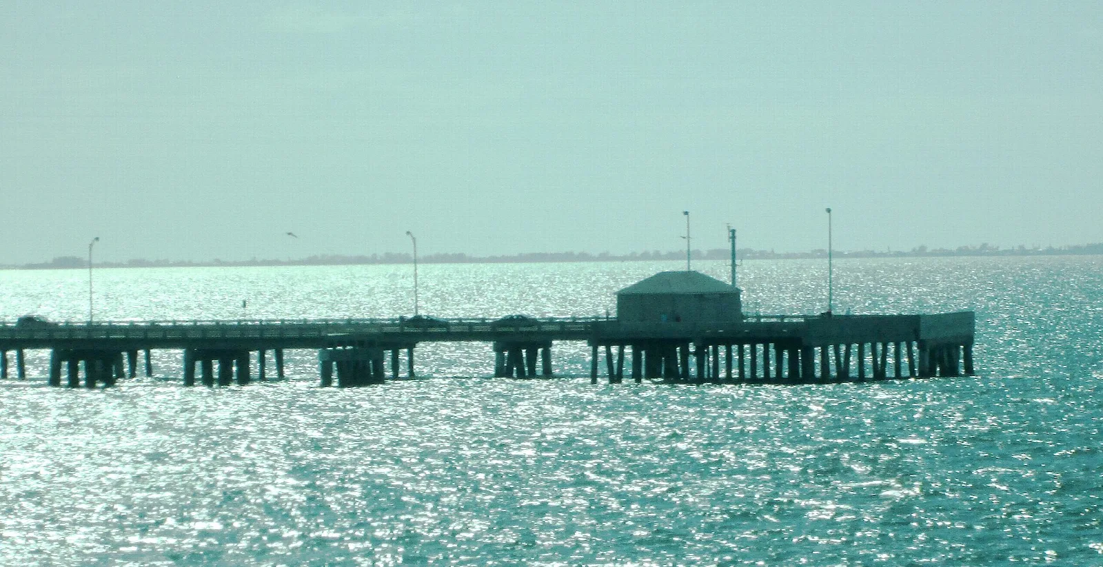 Long fishing pier with a small building out on sparkling water