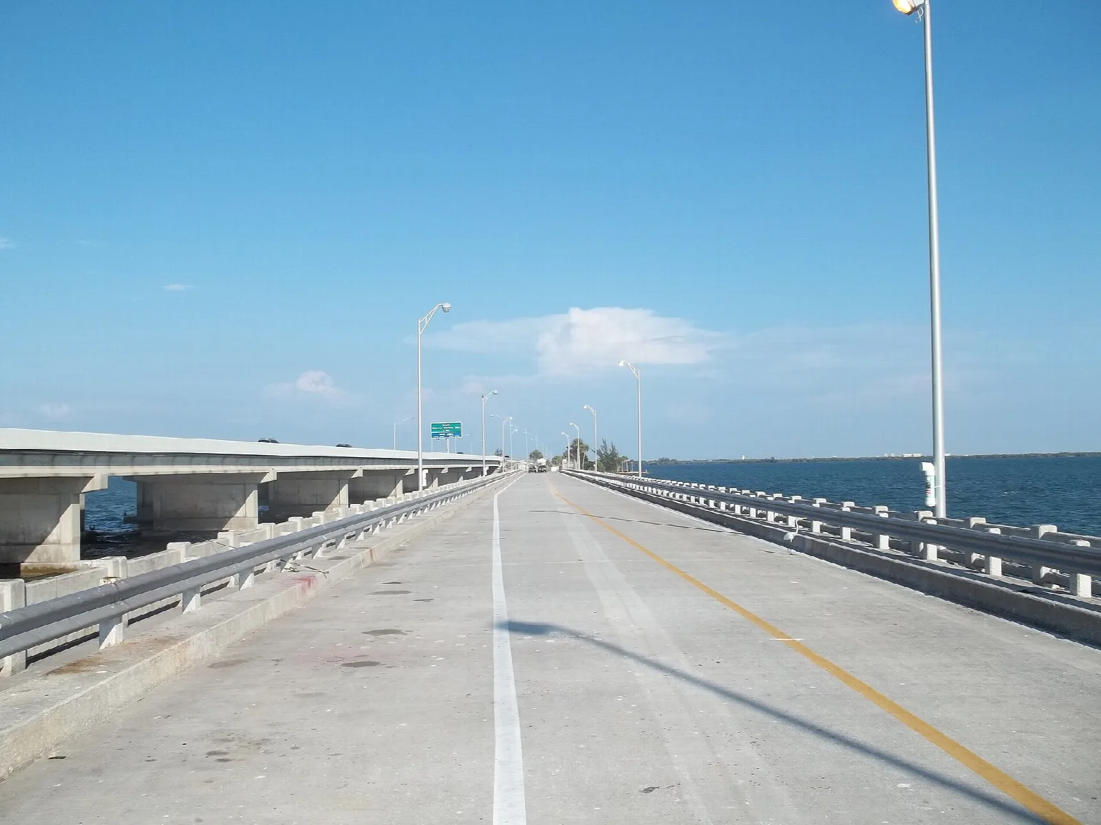 Empty fishing pier road running out over Tampa Bay under a blue sky with light poles