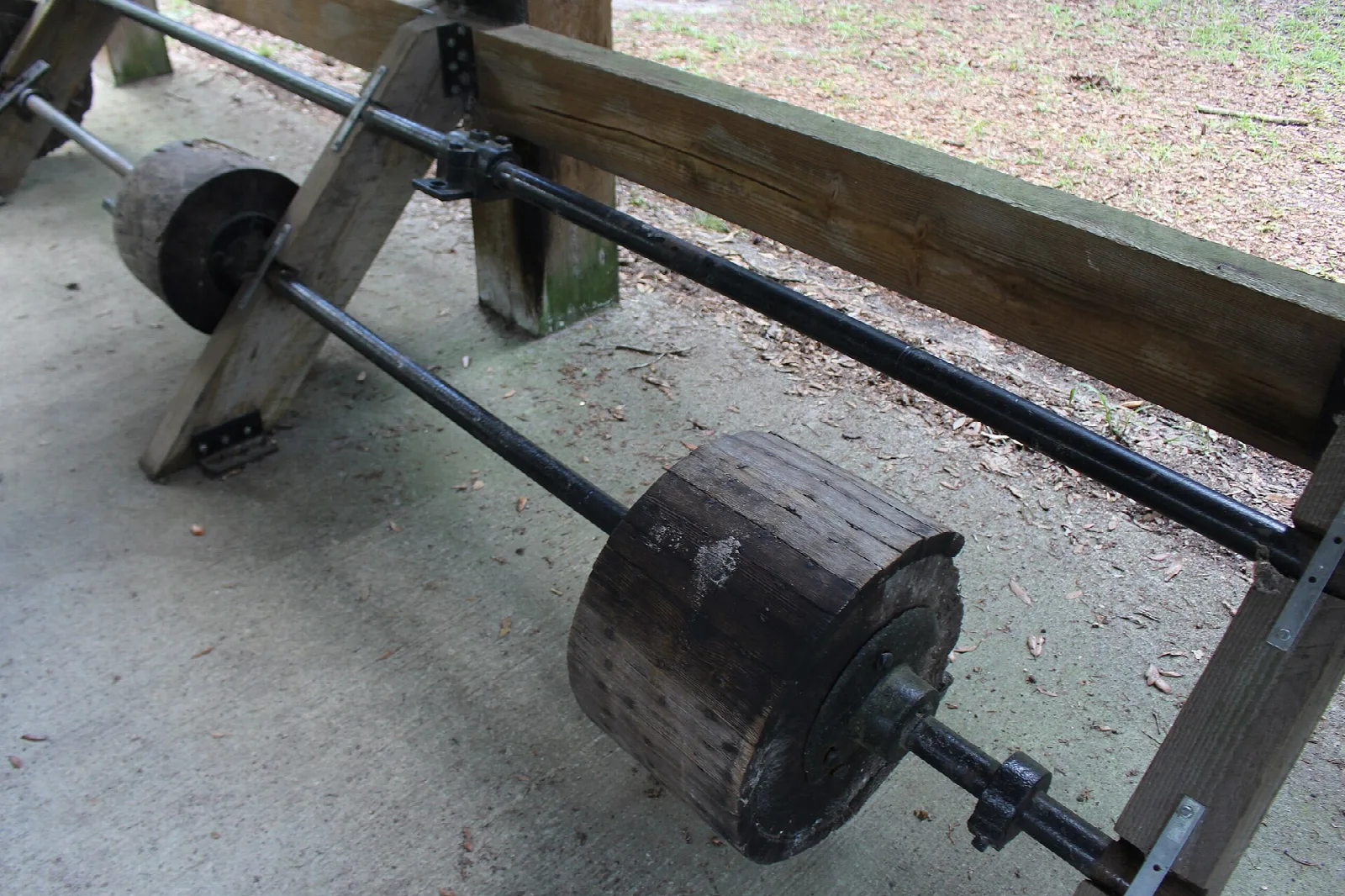Old wooden mill axle and wheels beside a timber frame