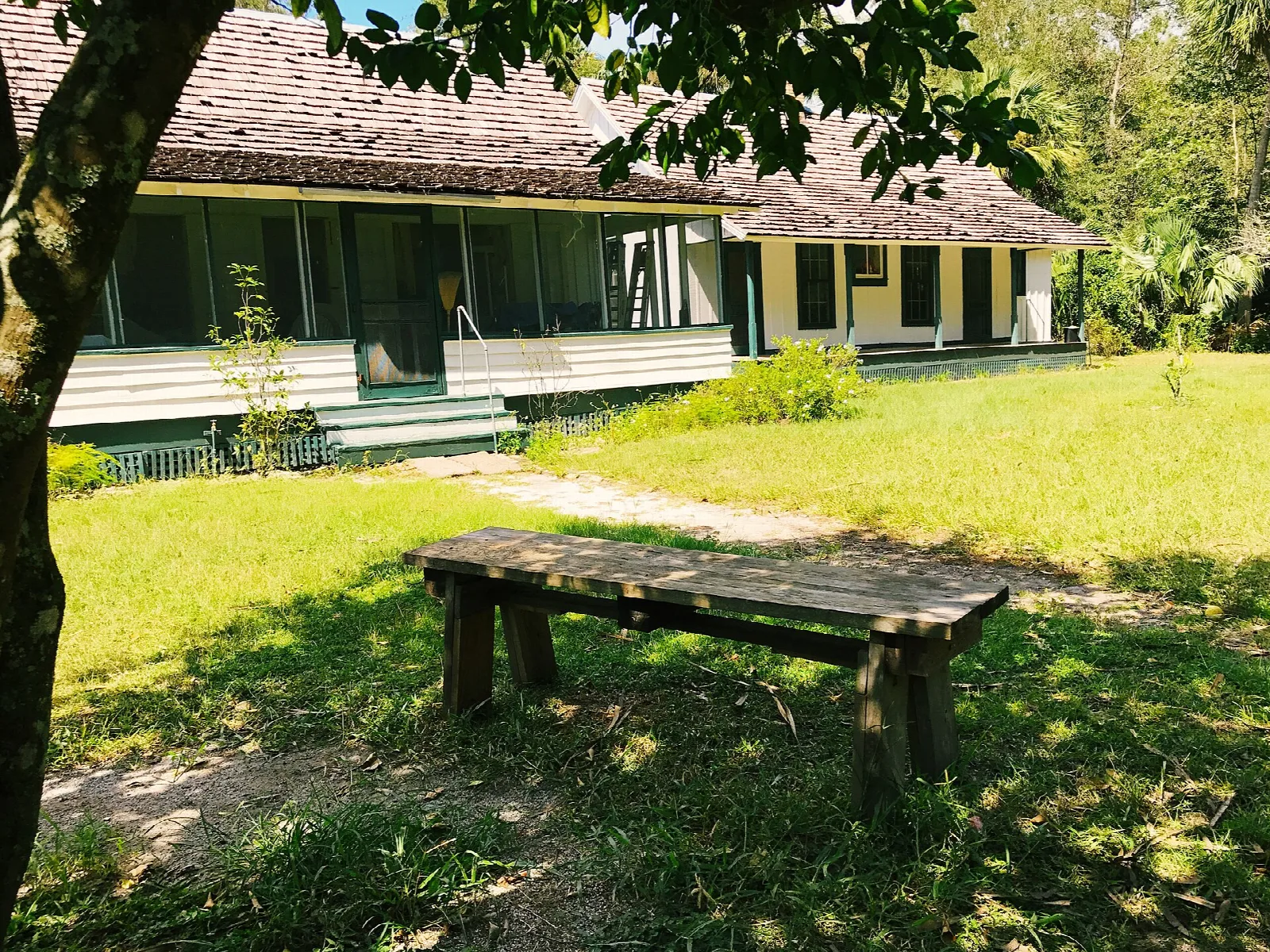 Farmhouse porch beyond a wooden bench on a green lawn