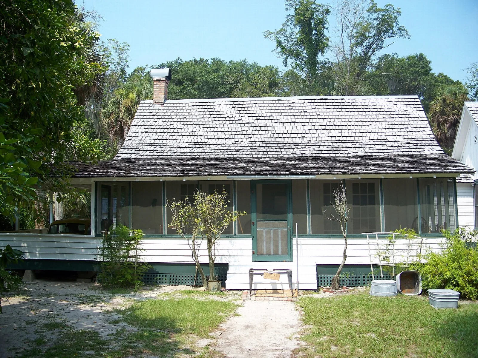 Wood farmhouse with a shingle roof and screened porch behind a sandy yard