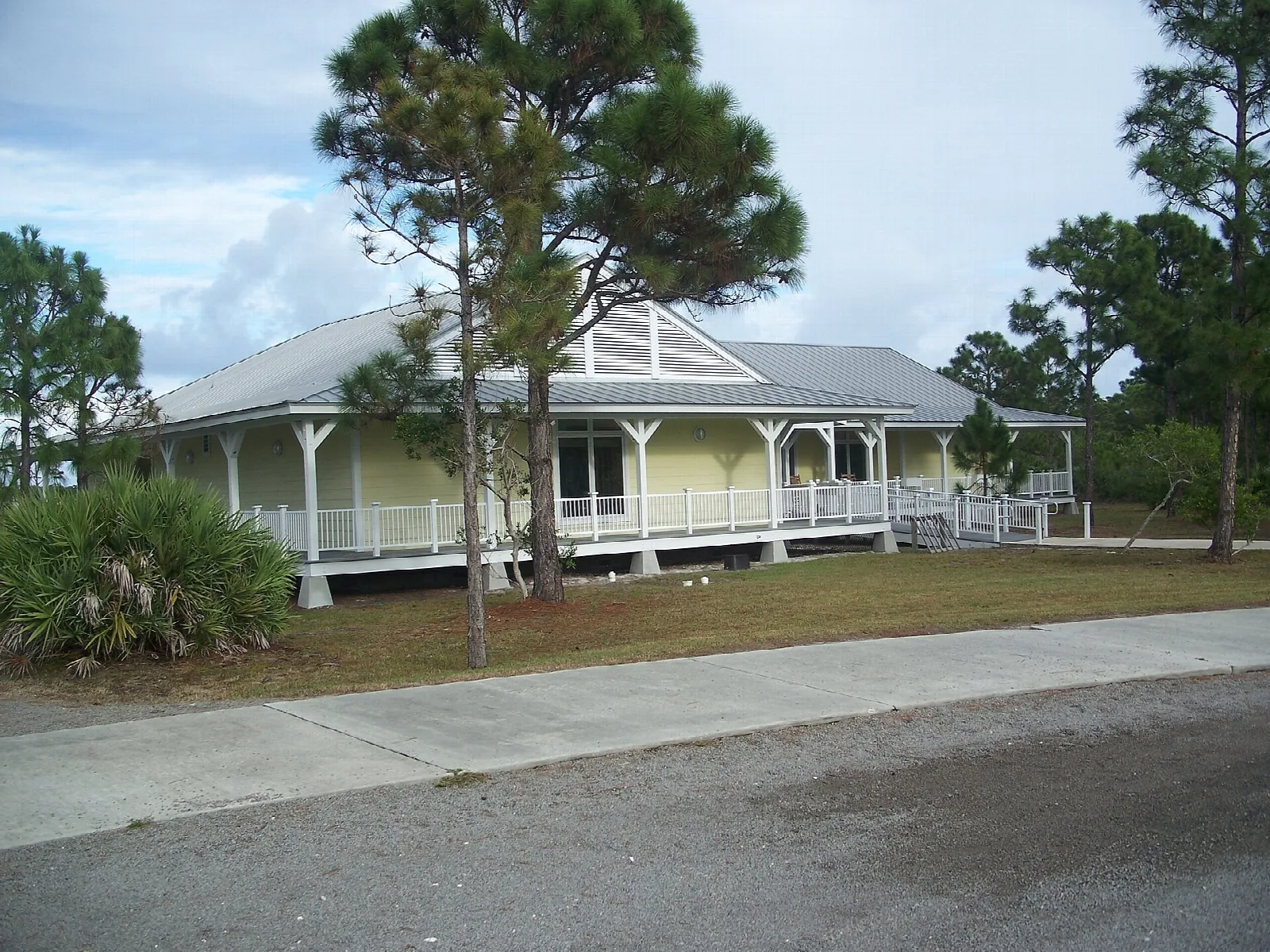 Yellow building with a wraparound porch among pines