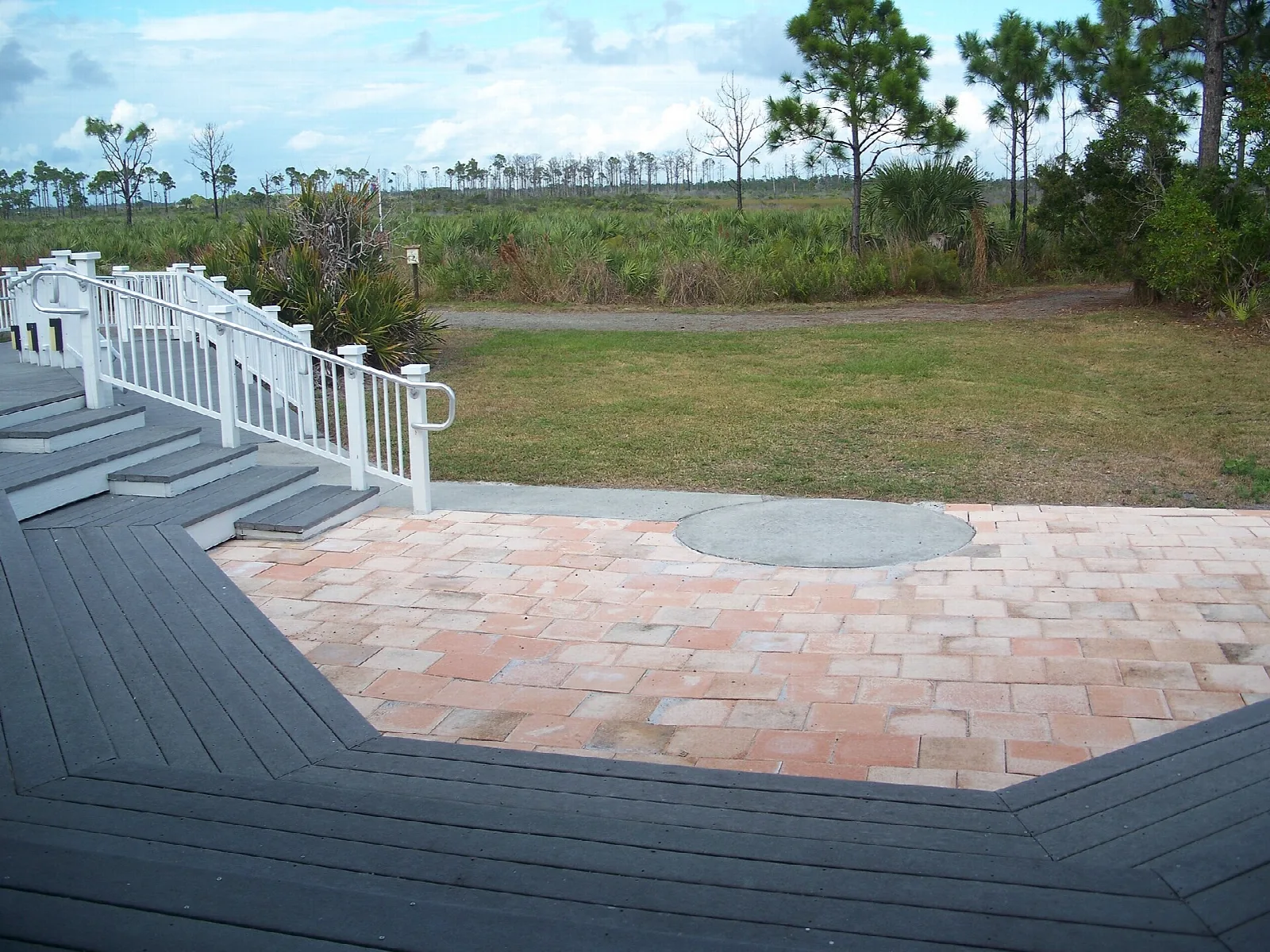 Brick patio and wooden deck with white rail beside open pine land
