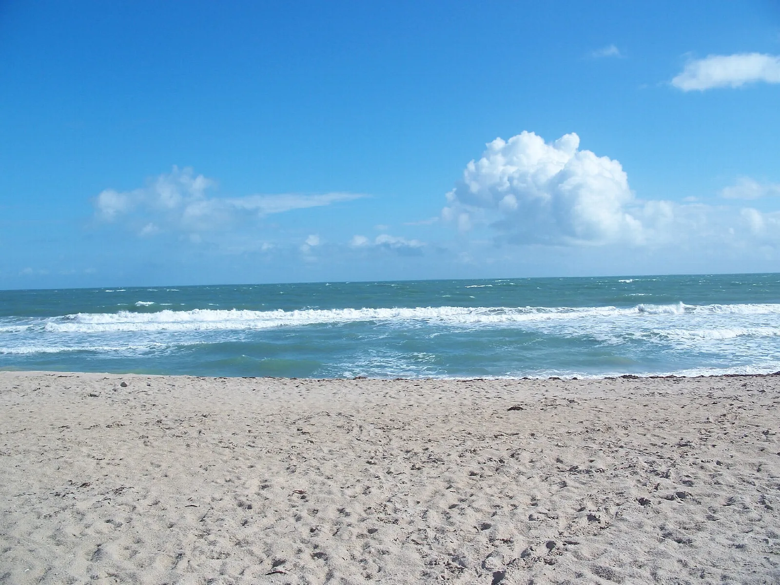 Waves rolling onto a wide sandy beach under blue sky and clouds