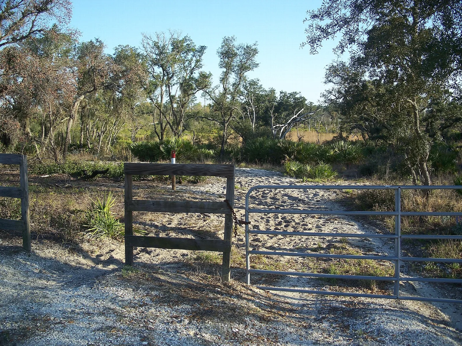 Wood and wire gate across a sandy track beside scrub trees