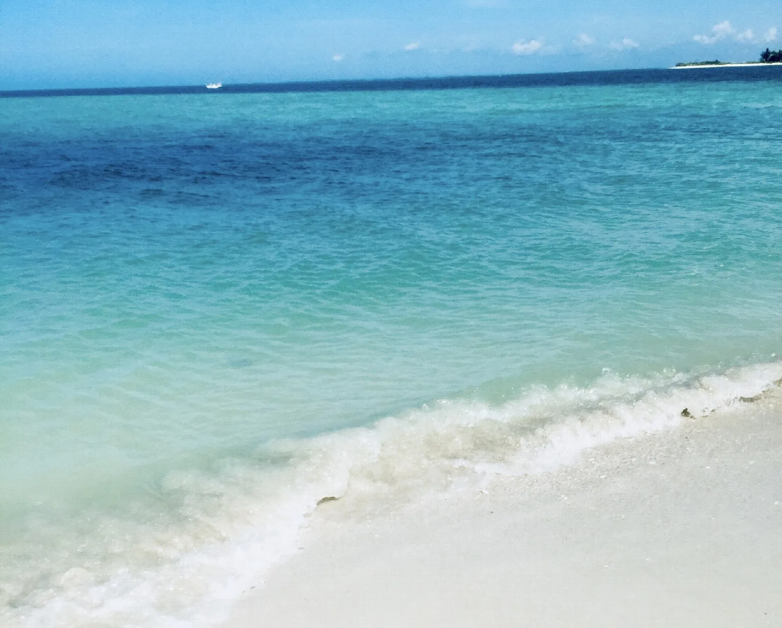 Clear turquoise water and white sand with a small wave