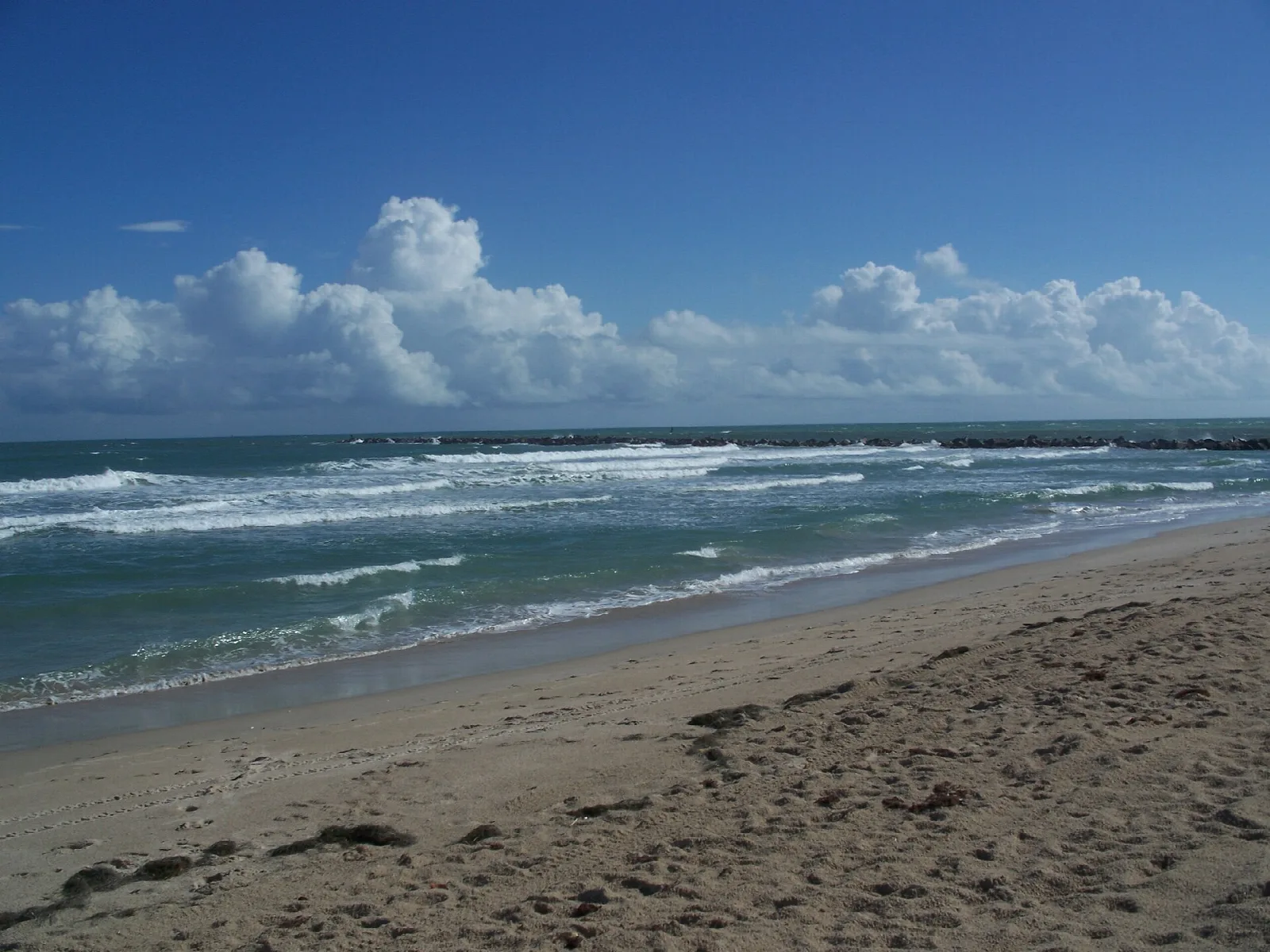 Waves breaking on a sandy beach under puffy clouds
