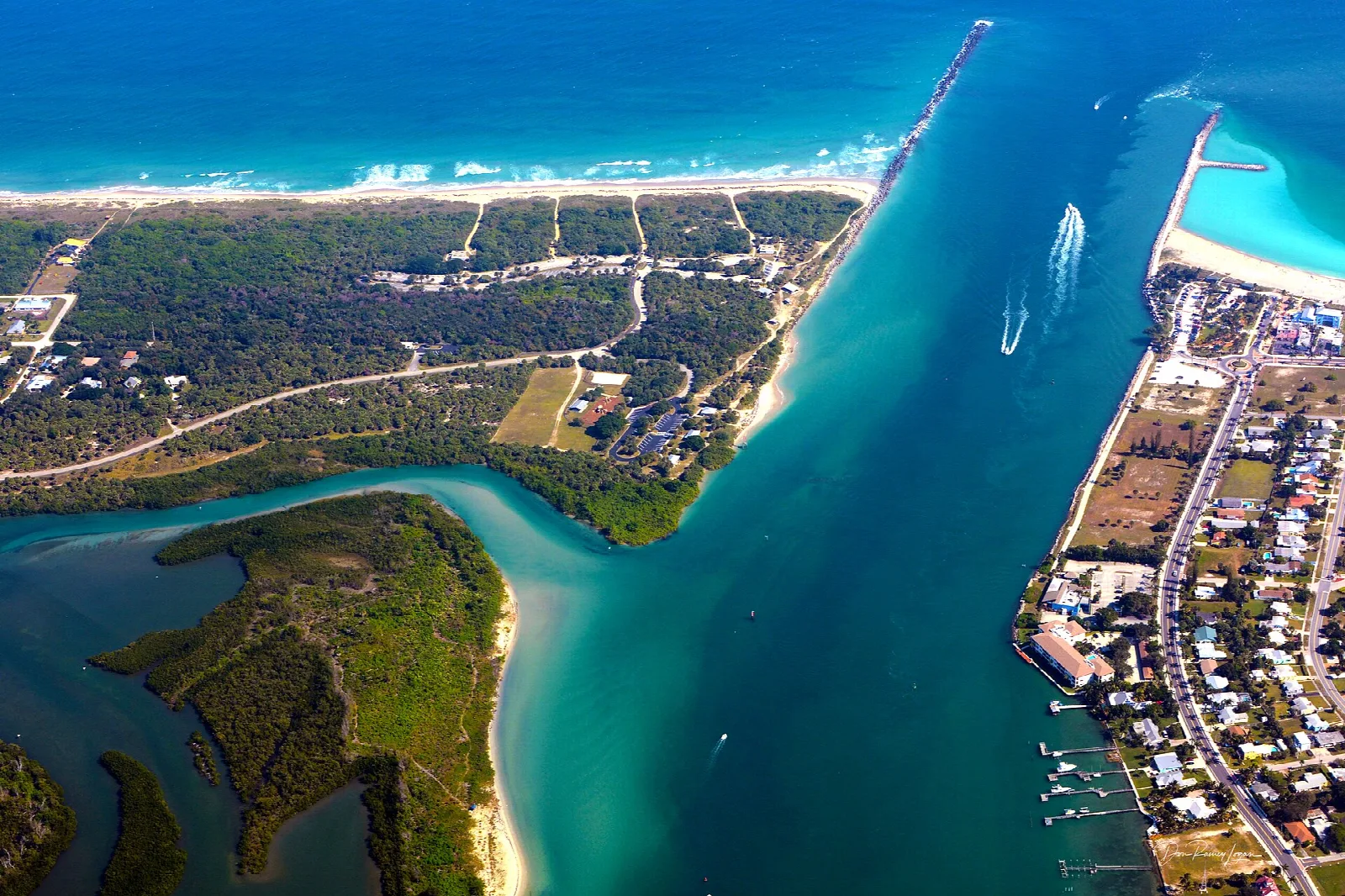 Aerial view of an inlet between two barrier islands with houses and green water