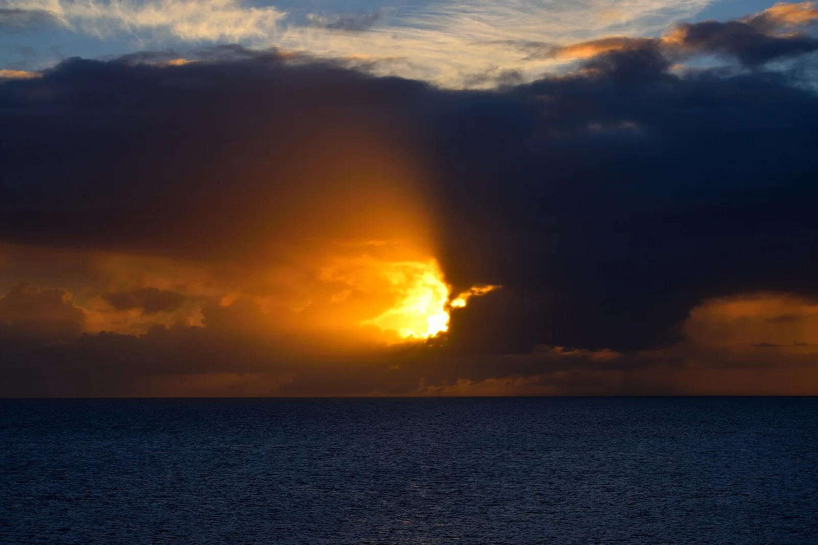 Sun breaking through dark clouds over the sea at sunset