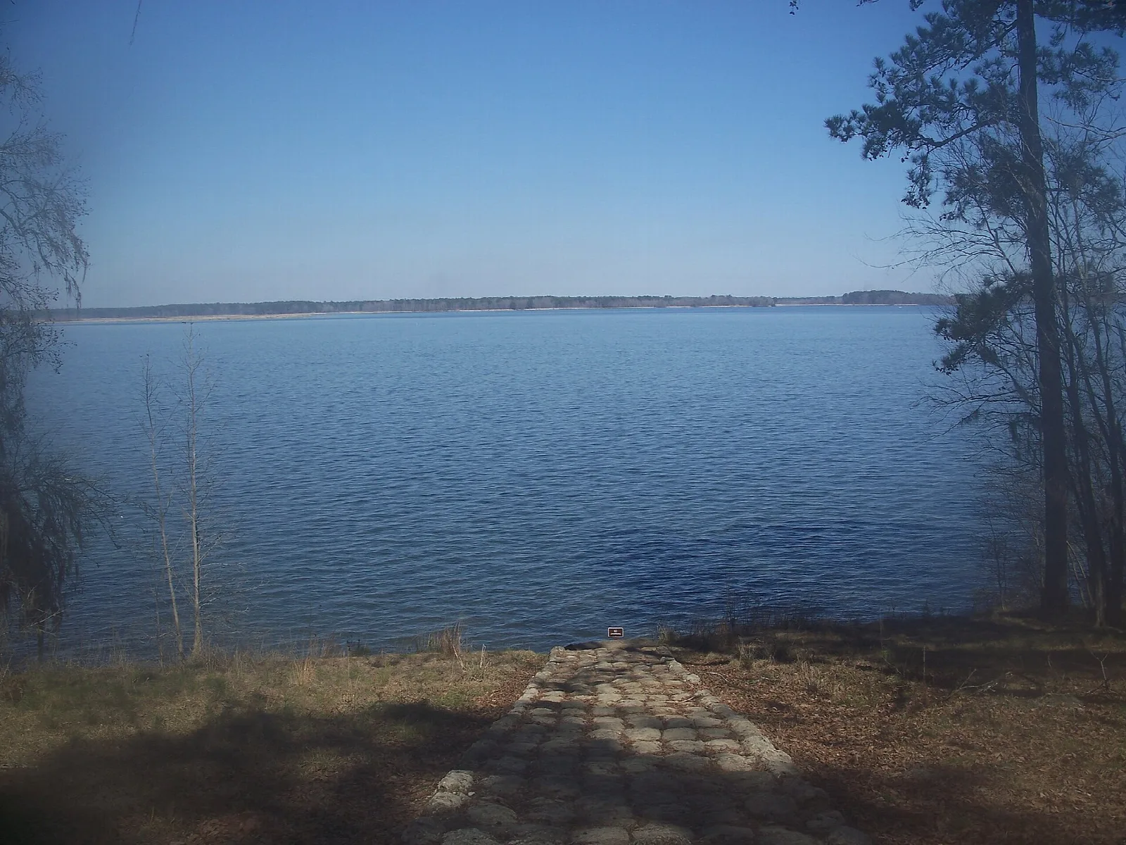Stone-edged path down to a wide lake with trees on the right