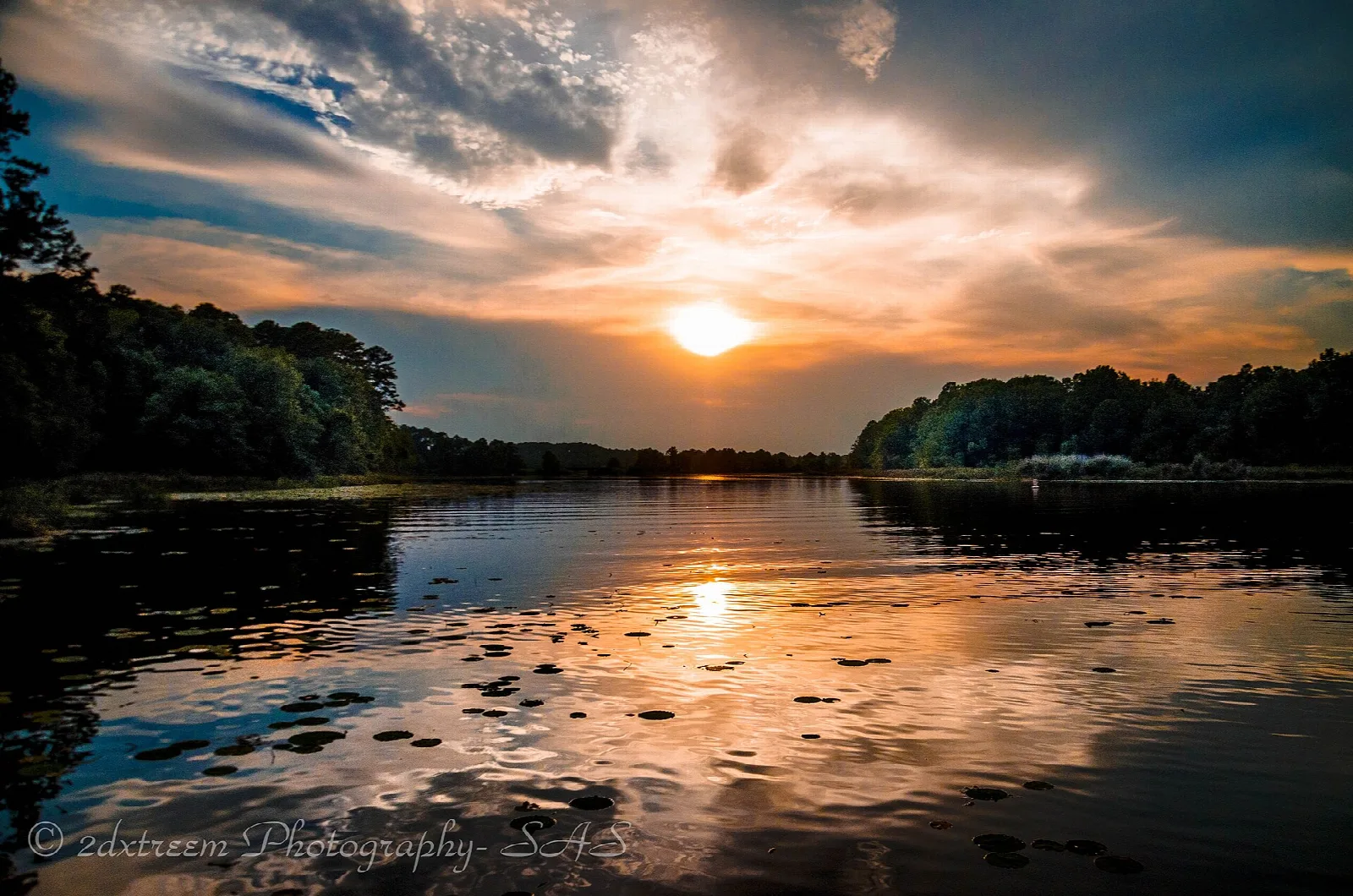 Orange sunset over a calm lake with tree-lined shores