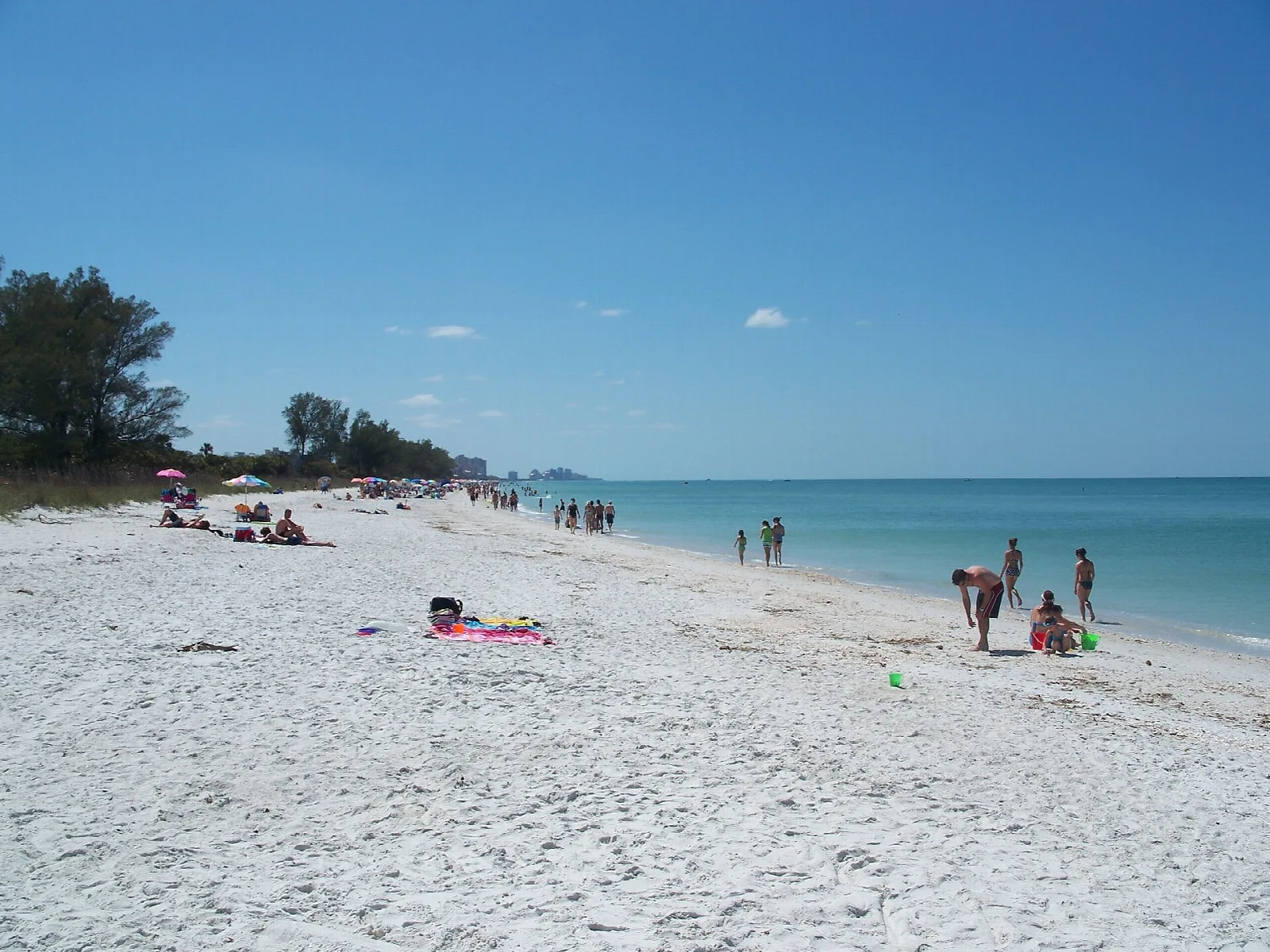 Long white beach with swimmers and a distant shoreline