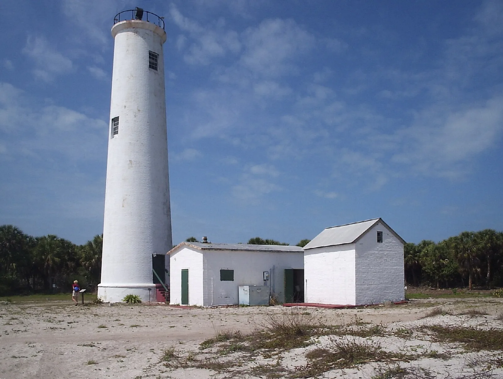 White lighthouse beside two small white buildings on sandy ground