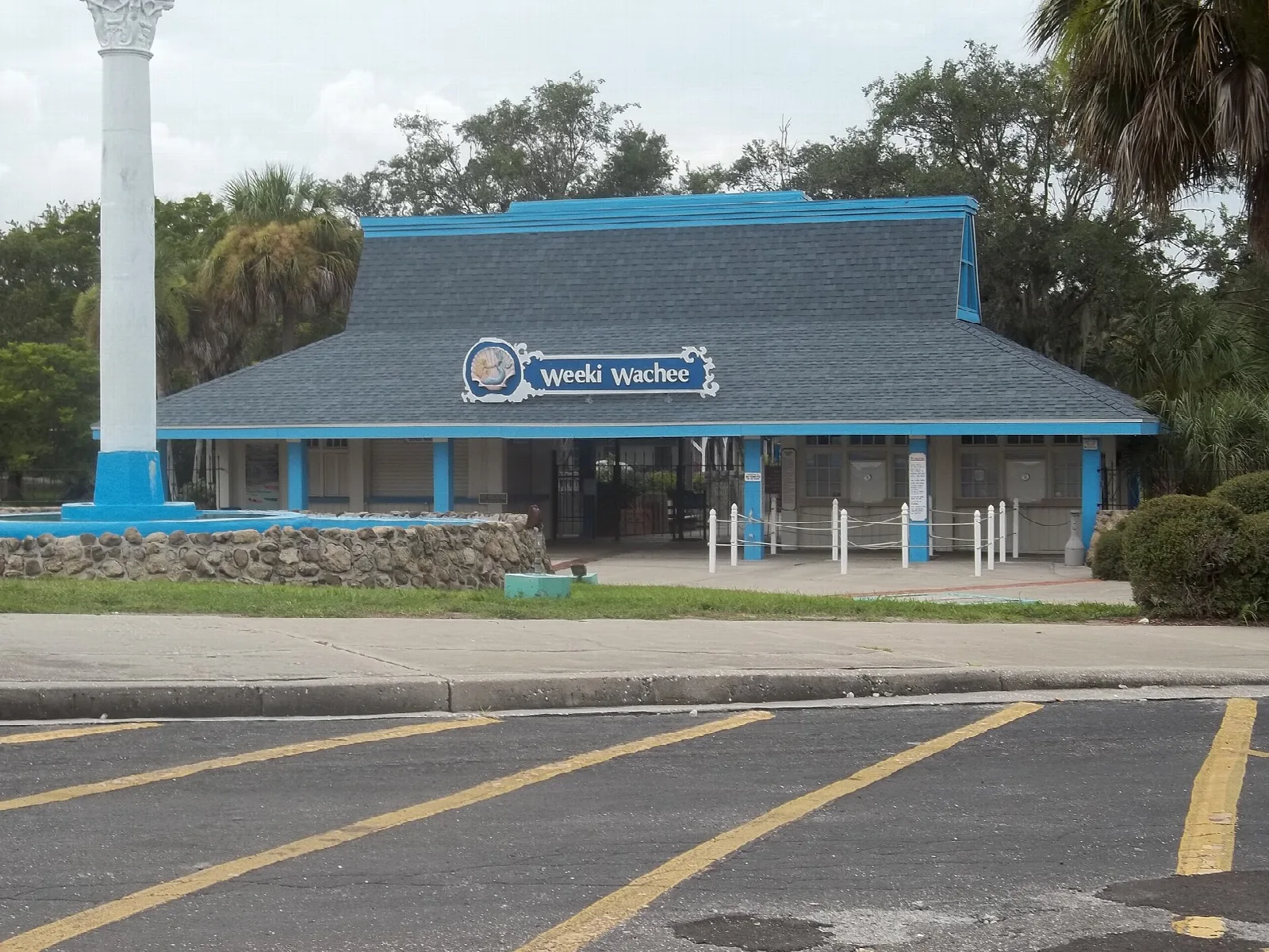 Blue-roofed low building with white column and parking lot