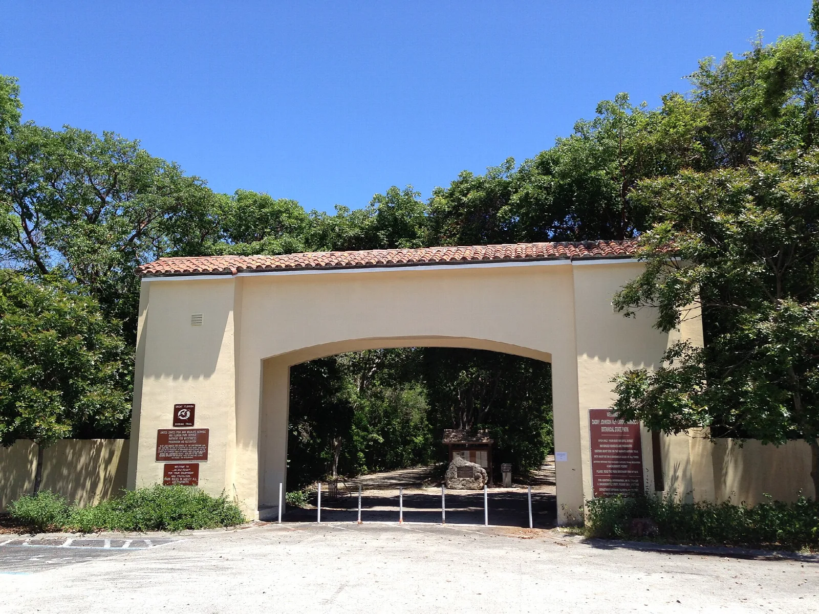 Tan arched gateway with tile roof among trees under blue sky
