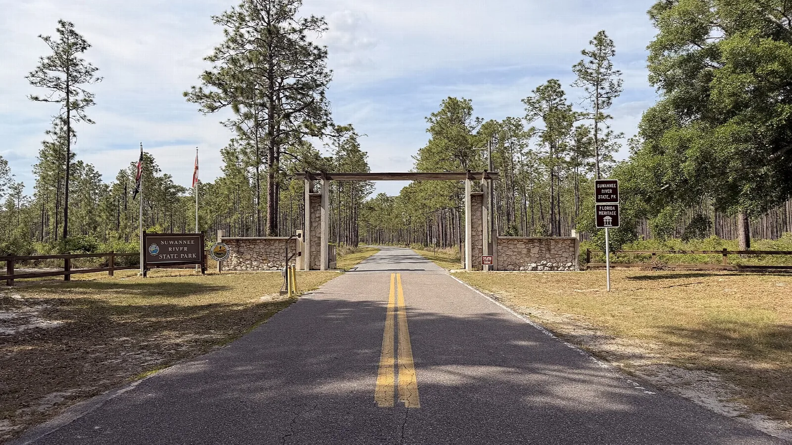 Paved road through pines to a wood entrance gate